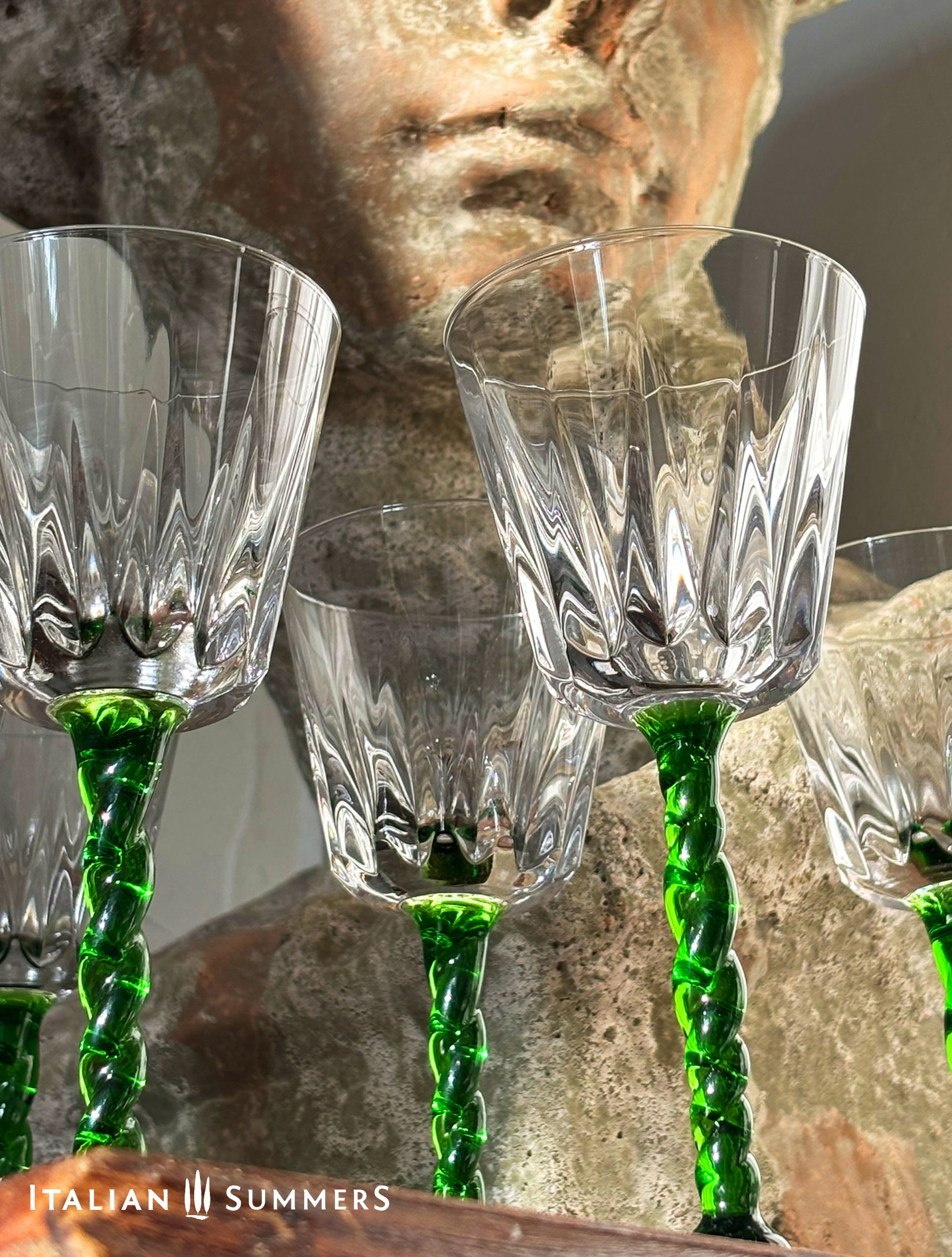 Crystal wine glasses with green stems in front of a stone sculpture