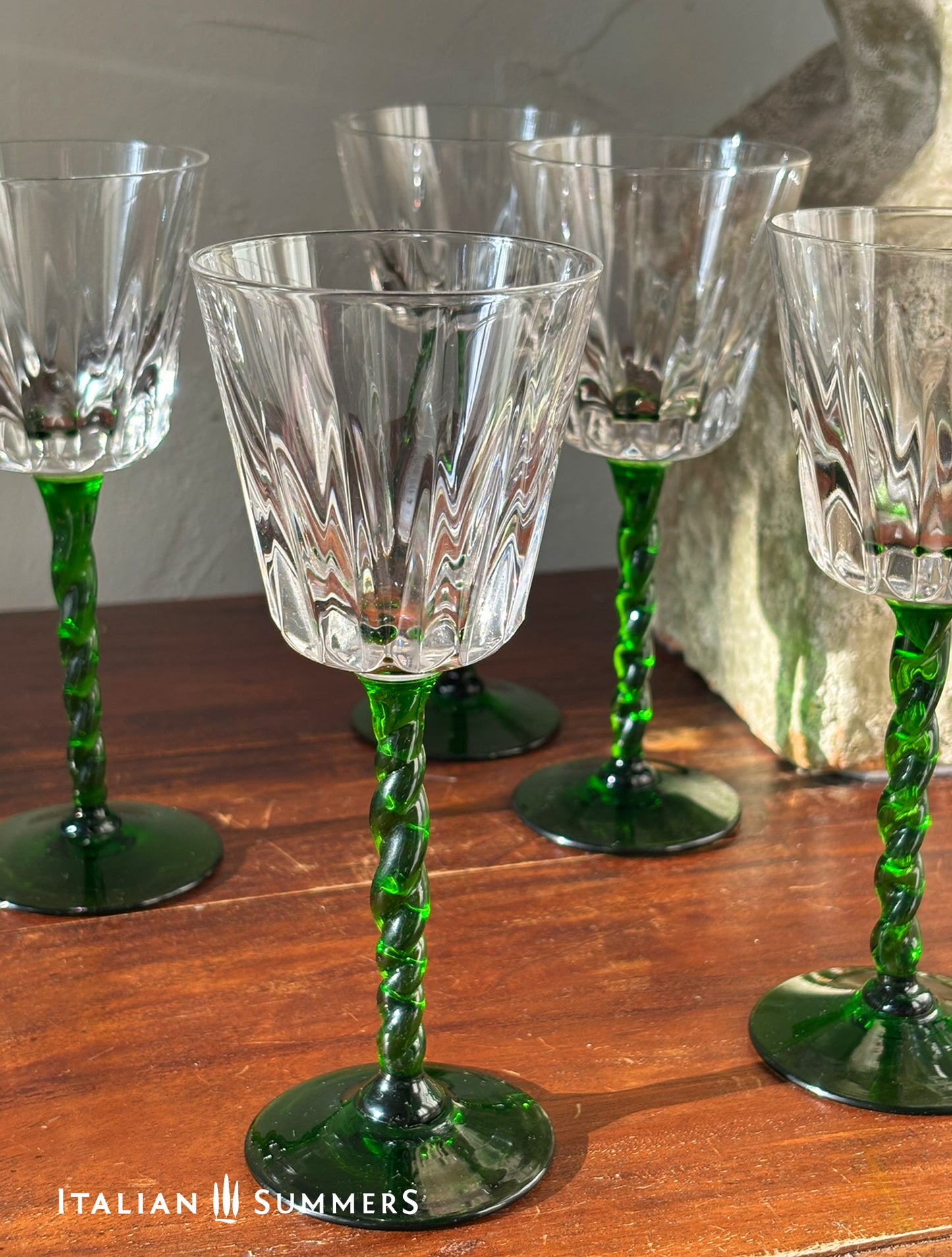 Set of crystal wine glasses with green stems on a wooden surface, featuring the brand 'Italian Summers'.