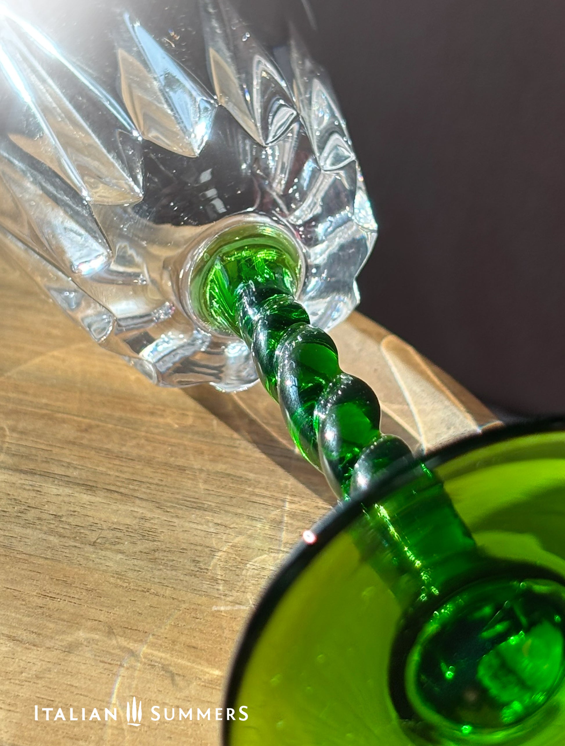 Close-up of a green glass-stemmed crystal wine glass bottle on a wooden surface, featuring 'Italian Summers' branding.