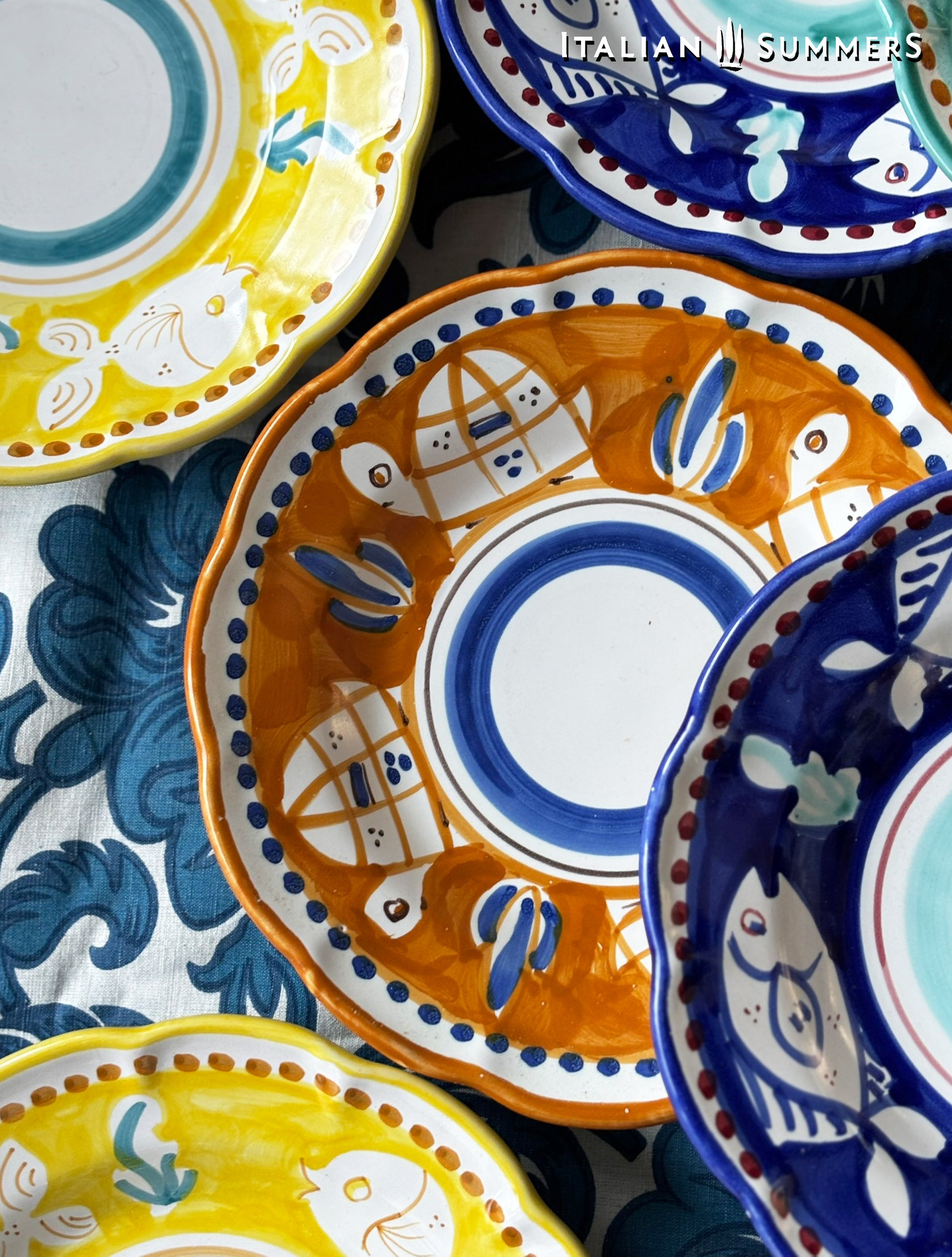  A group of multi-Colored hand-painted Vietri Pasta Plates with fish theme decorations from the Amalfi Coast on a blue and white tablecloth