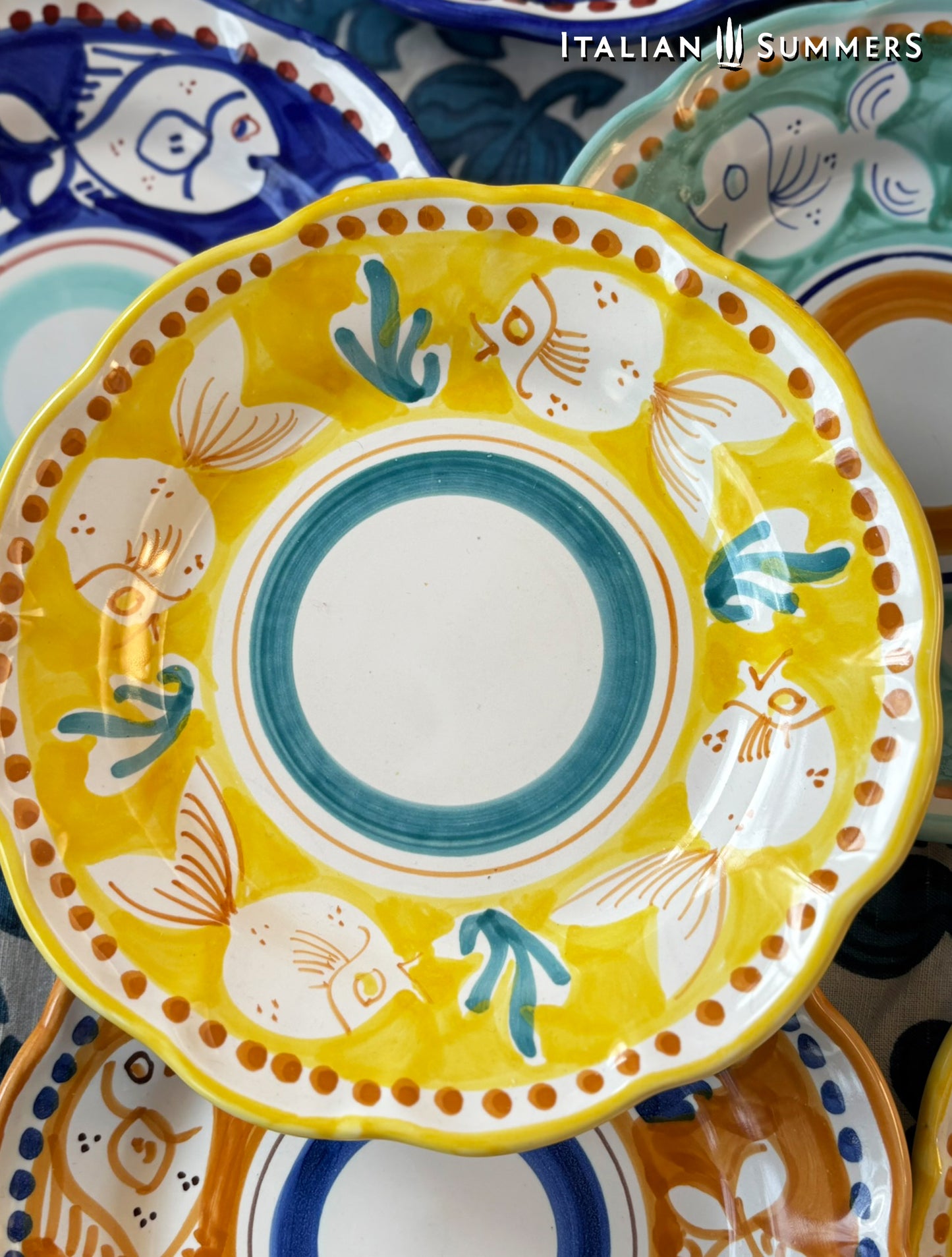 Deatail of a group of multi-Colored hand-painted Vietri Pasta Plates with fish theme decorations from the Amalfi Coast on a blue and white tablecloth