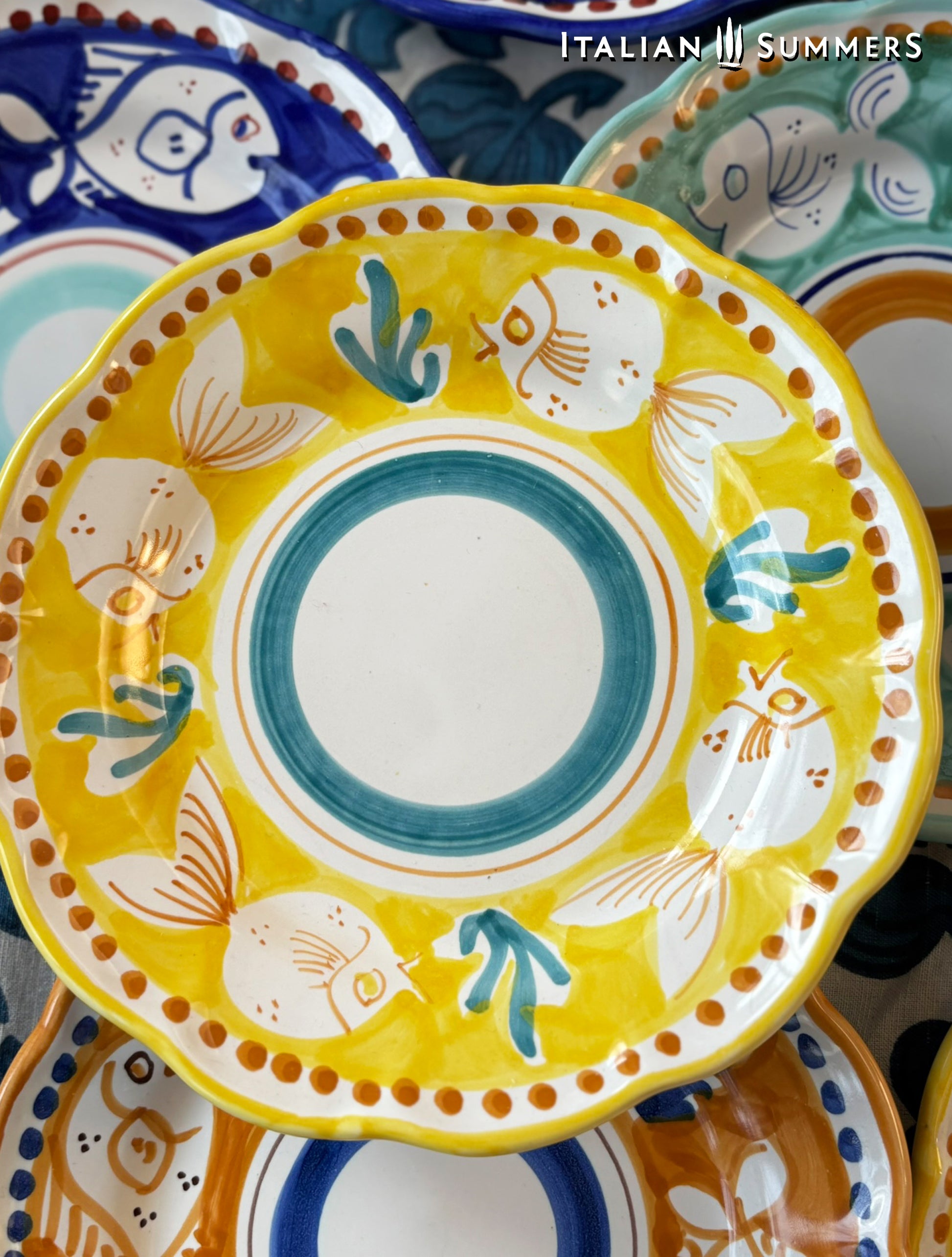 Deatail of a group of multi-Colored hand-painted Vietri Pasta Plates with fish theme decorations from the Amalfi Coast on a blue and white tablecloth