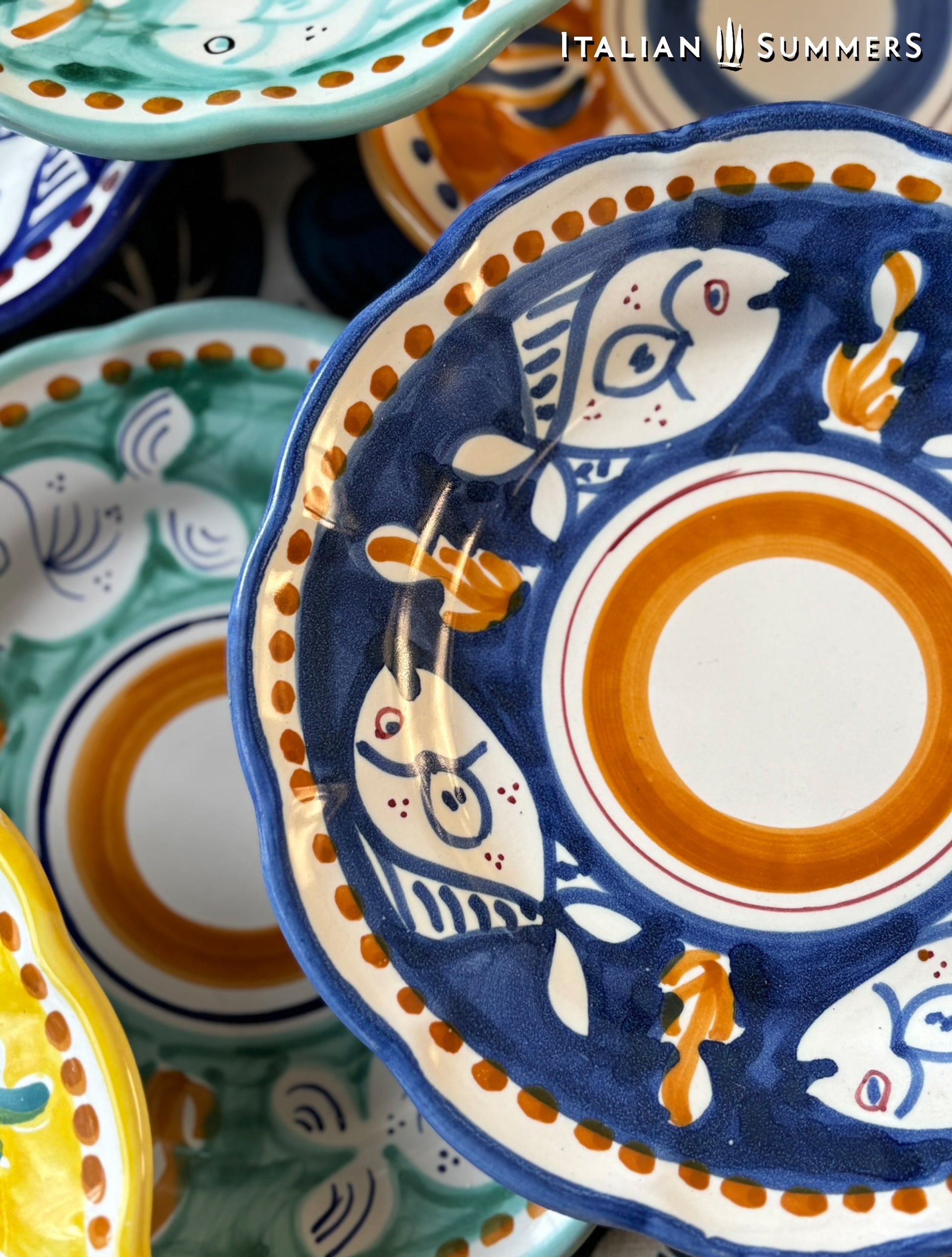 Close-up of a group of multi-Colored hand-painted Vietri Pasta Plates with fish theme decorations from the Amalfi Coast on a blue and white tablecloth