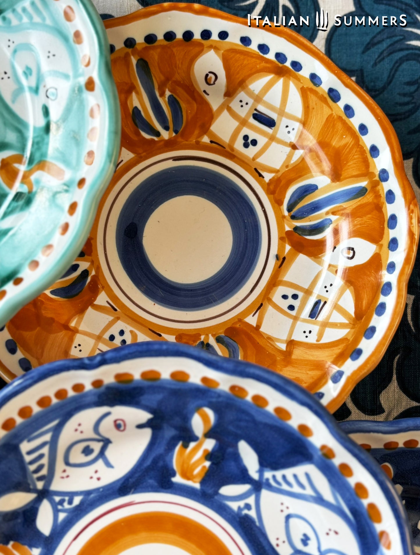  Detail of a group of multi-Colored hand-painted Vietri Pasta Plates with fish theme decorations from the Amalfi Coast on a blue and white tablecloth