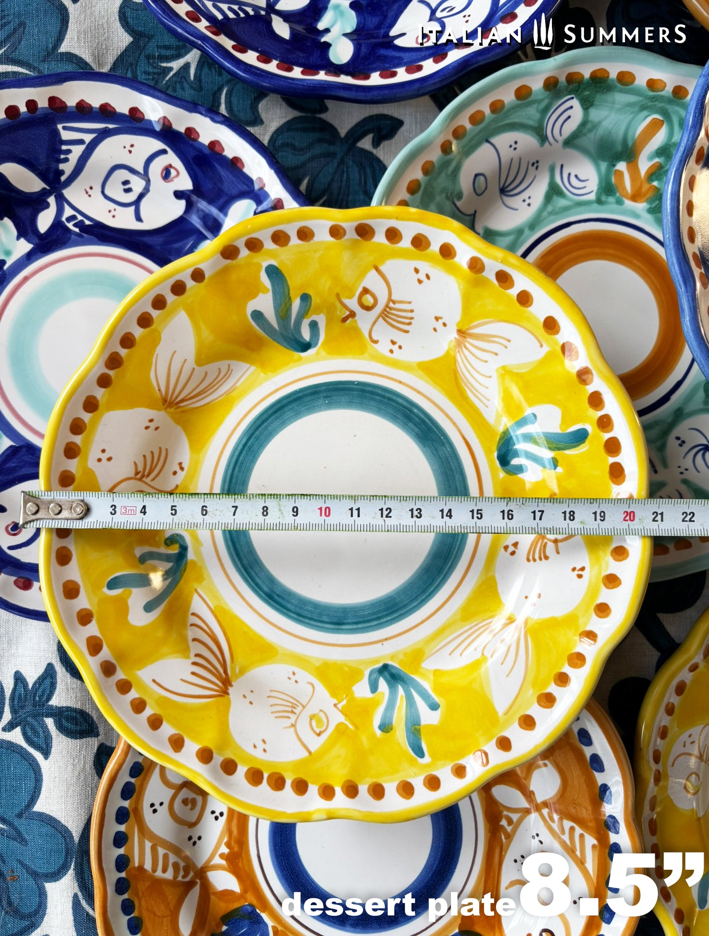 close-up of a bright yellow plate in a group of multi-Colored hand-painted Vietri Pasta Plates with fish theme decorations from the Amalfi Coast on a blue and white tablecloth