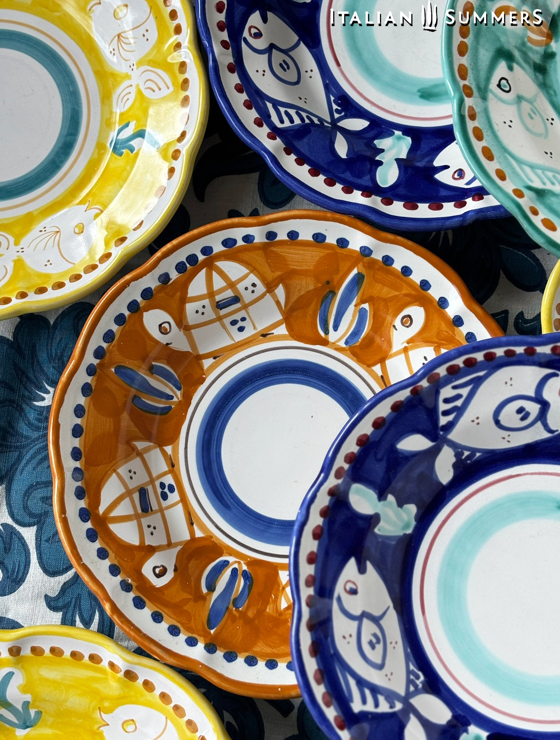A close-up of A group of Colorful hand-painted Vietri Plates  with fish theme decorations from the Amalfi Coast o a blue and white tablecloth