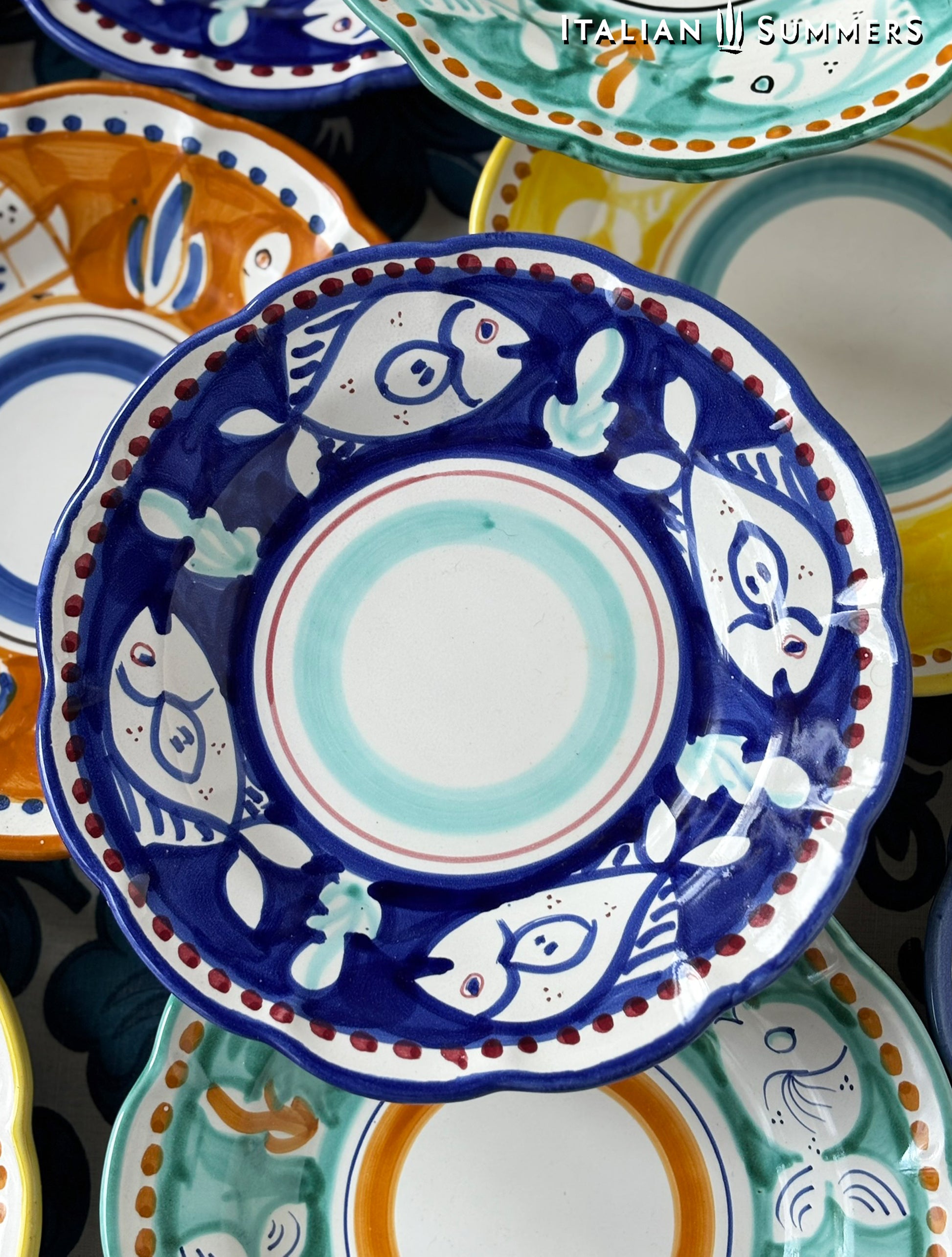 deatail of a A close-up of A group of Colorful hand-painted Vietri Pasta Plate with fish theme decorations from the Amalfi Coast on a blue and white tablecloth