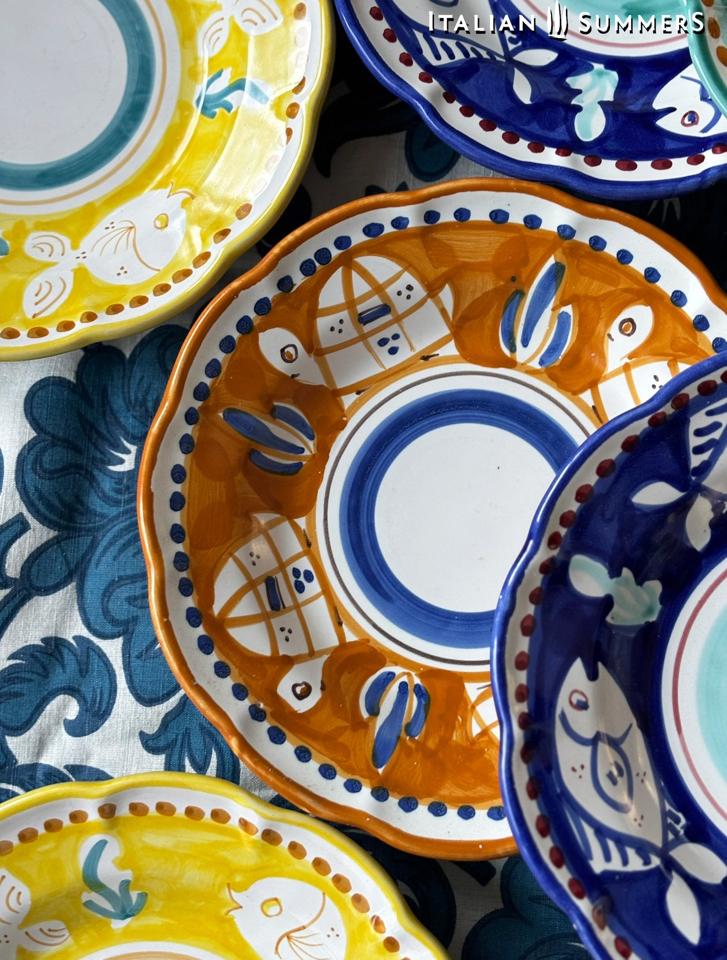 A detail of a A close-up of A group of Colorful hand-painted Vietri Pasta Plate with fish theme decorations from the Amalfi Coast on a blue and white tablecloth