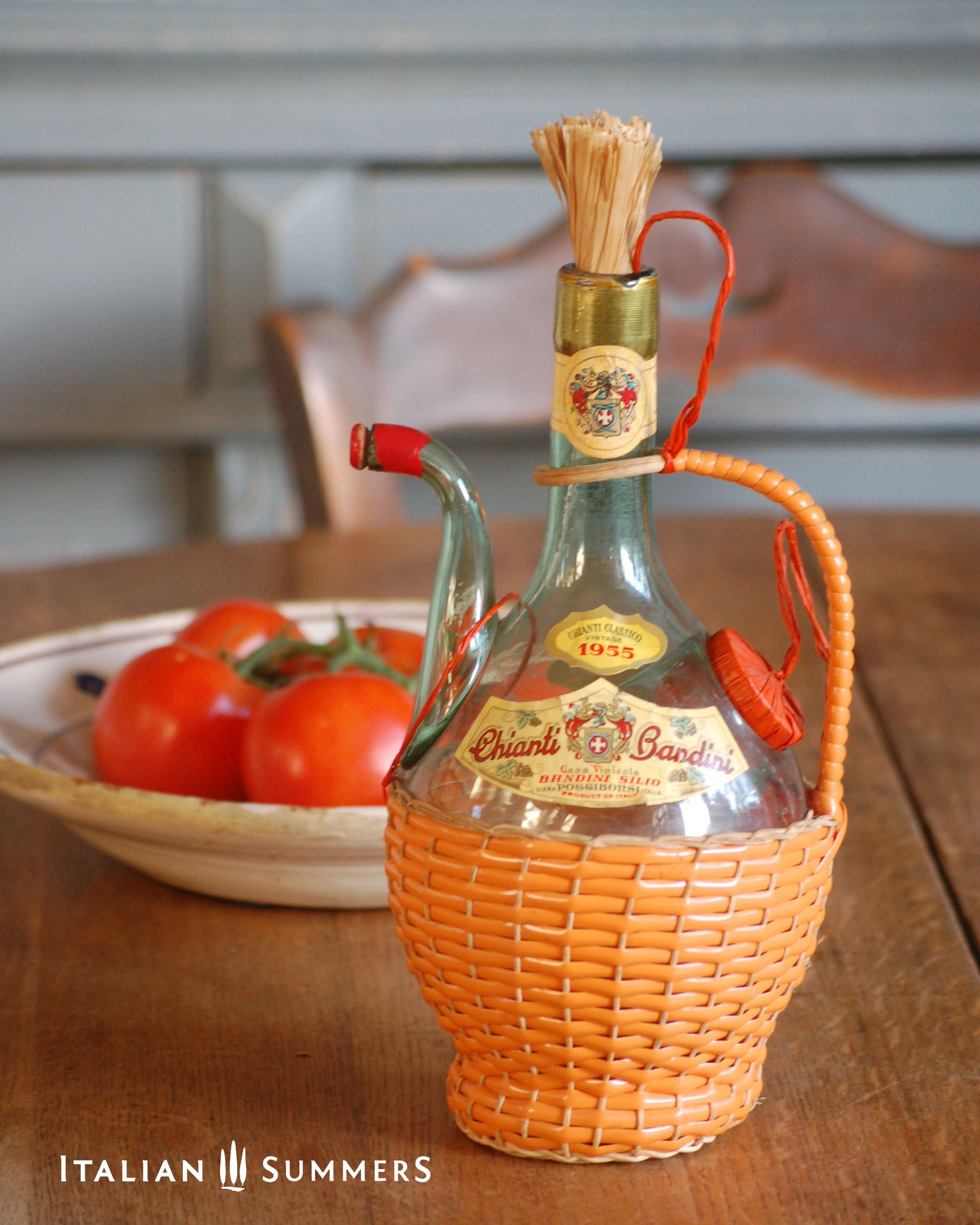 Vintage wine bottle with a wicker holder on a wooden table with tomatoes in the background.