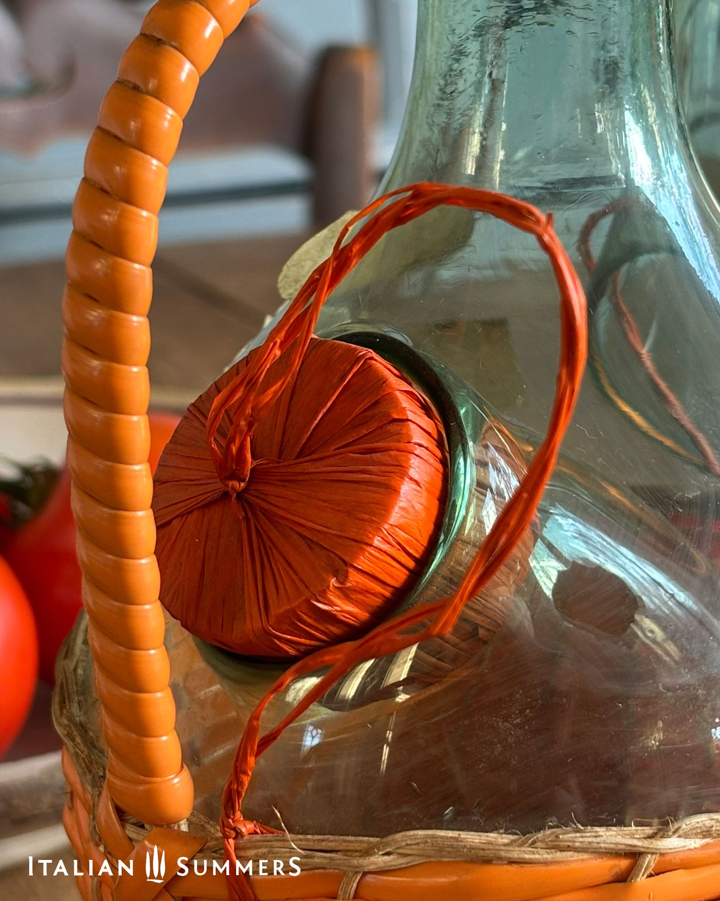 Glass bottle with orange cap and handle, tied with red string, on a blurred background.