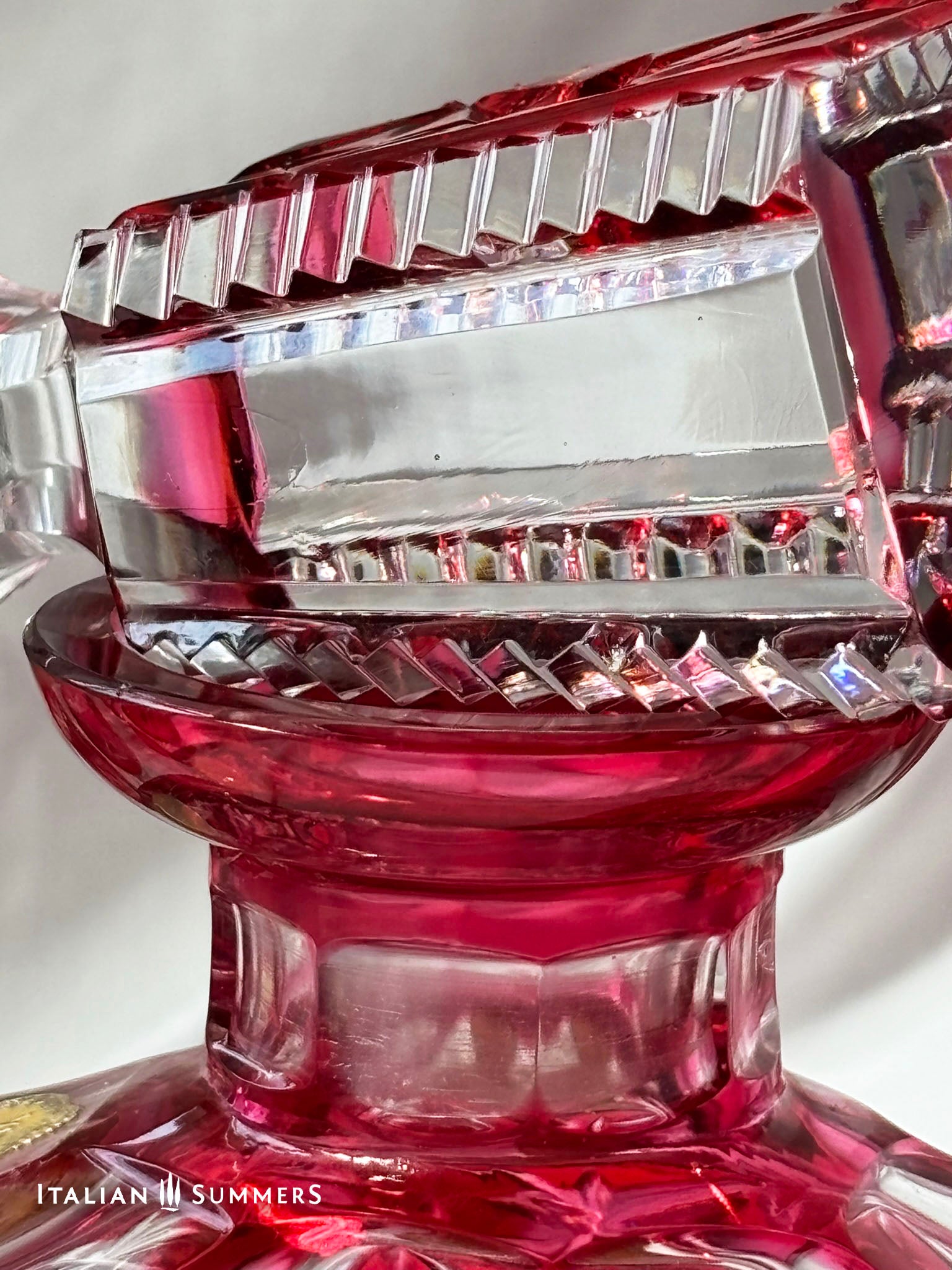 deail of a stopper from a cut crystal cranberry-red decanter The glassware is displayed on a white surface. The text "ITALIAN 