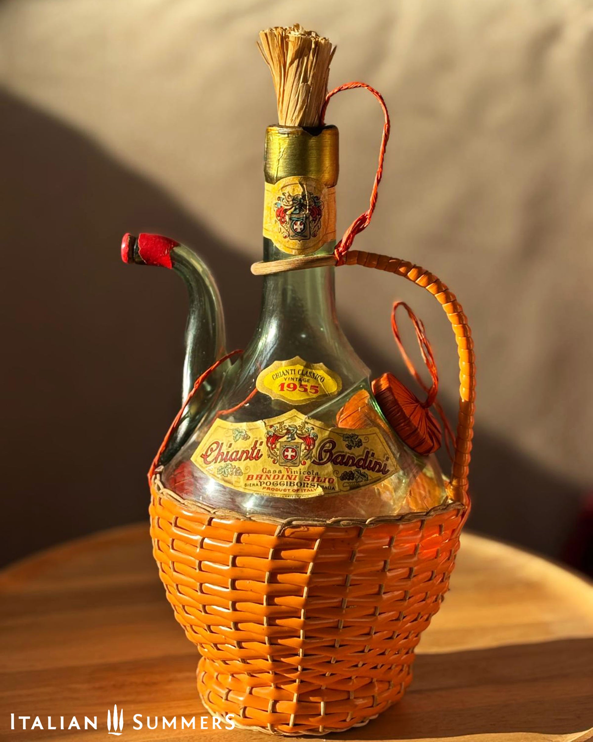 Vintage wine bottle with basket on a wooden surface, featuring the brand 'Chianti Bandini'.