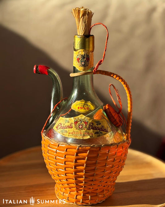 Vintage wine bottle with basket on a wooden surface, featuring the brand 'Chianti Bandini'.
