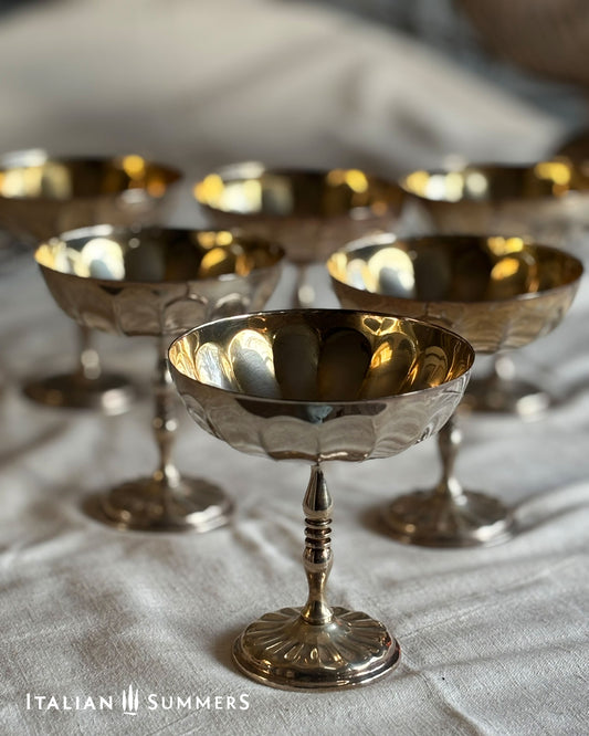 Set of silver and gold compote dishes on a textured surface with 'Italian Summers' branding.