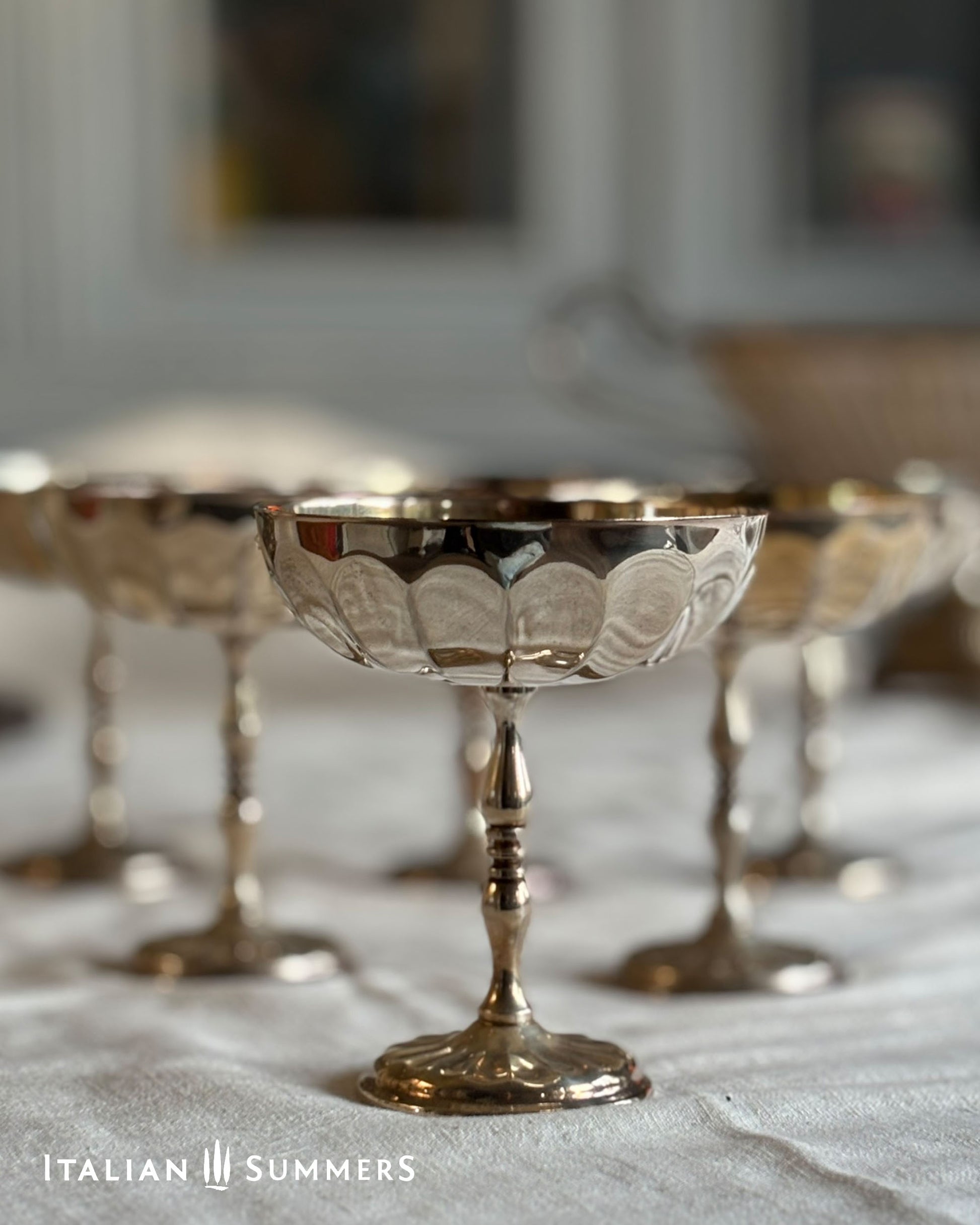 Silver pedestal bowls with intricate designs on a textured surface, branded 'Italian Summers'.