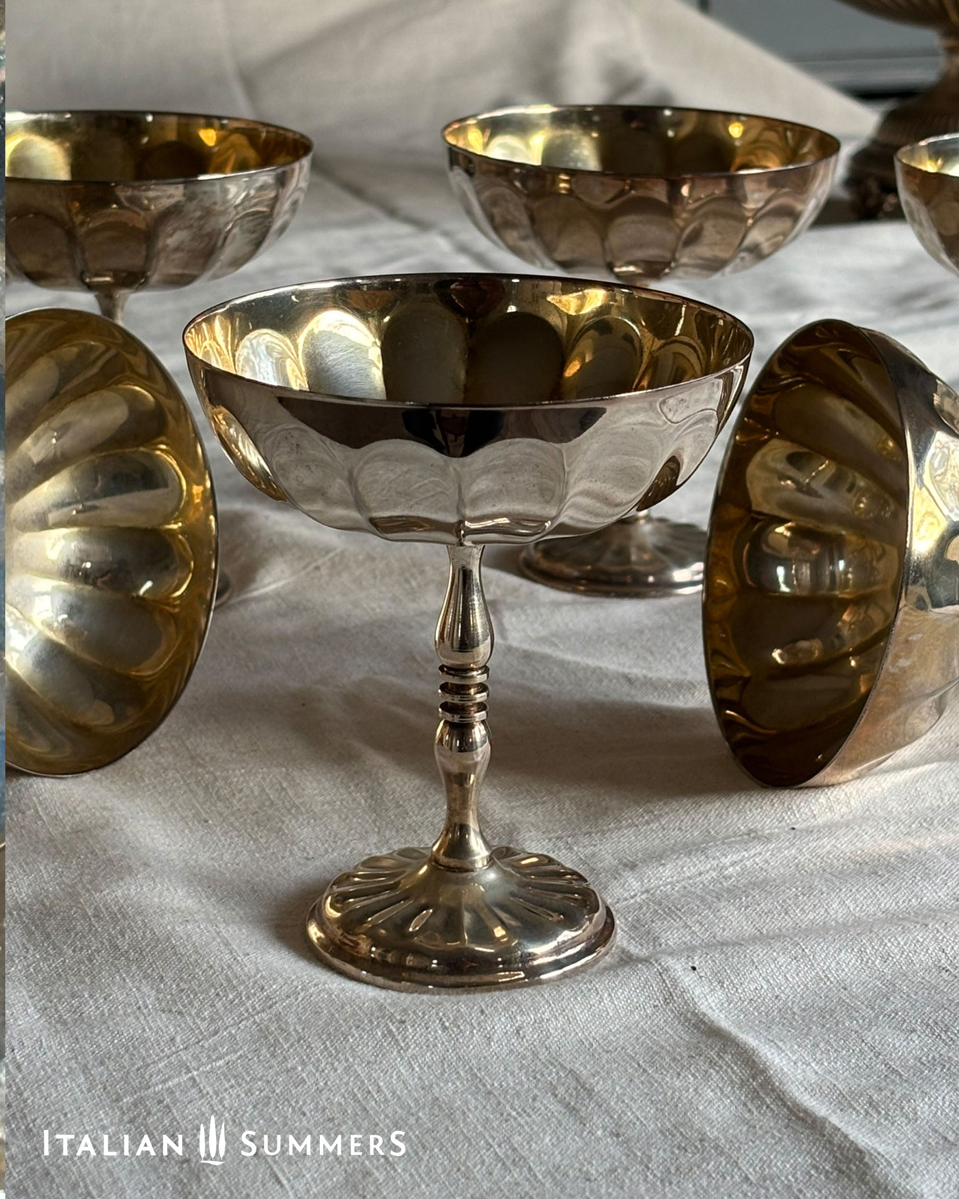 Set of silver and gold plated champagne coupes with a central stand on a textured surface, featuring 'Italian Summers' branding.