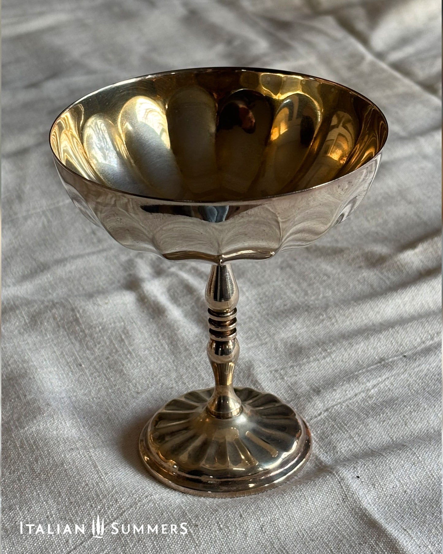 Gold and silver goblet on a textured fabric background with 'Italian Summers' branding.