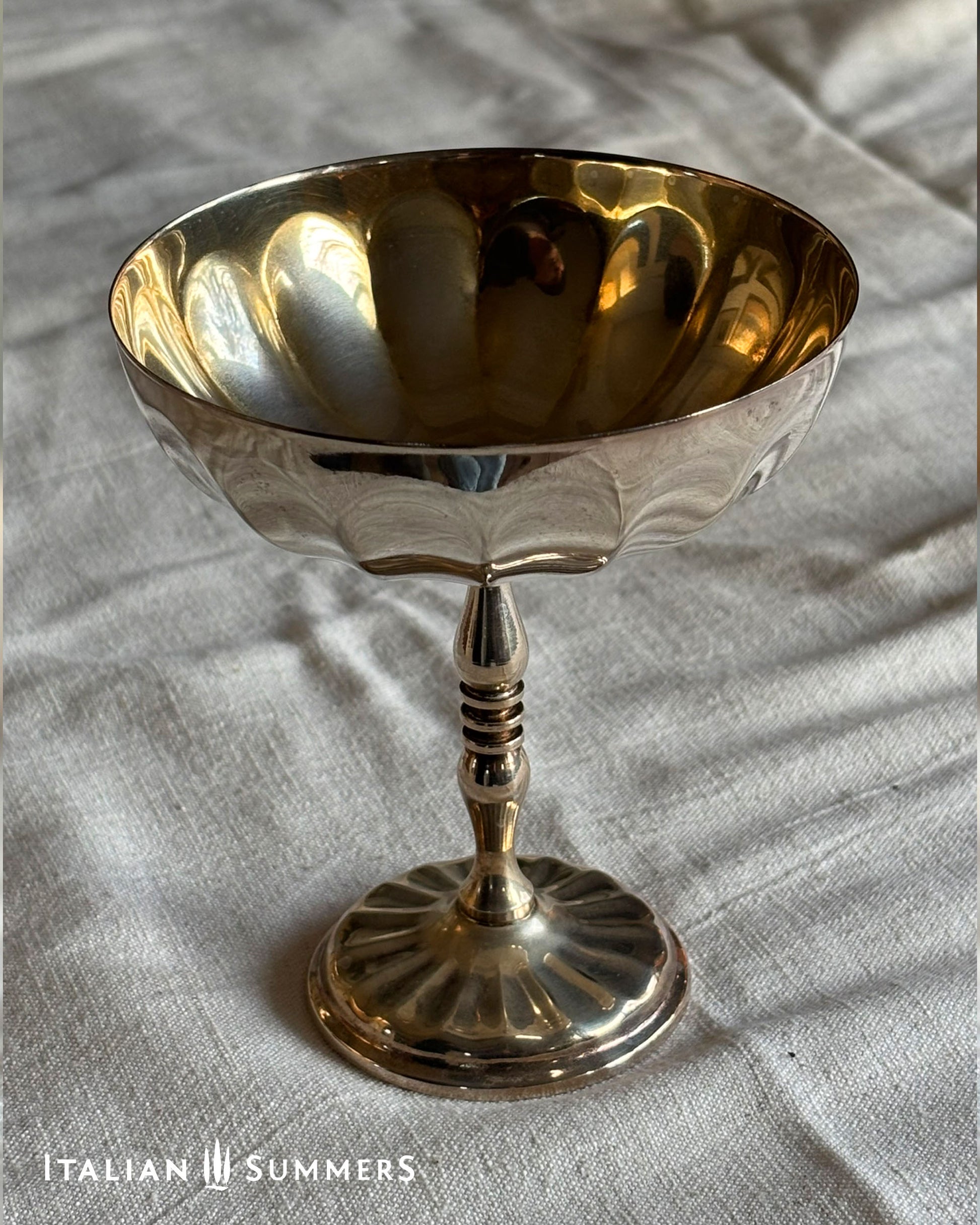 Gold and silver goblet on a textured fabric background with 'Italian Summers' branding.