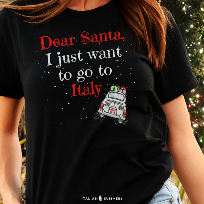 Italy Christmas Black T shirt featuring a cute vintage Fiat car loaded with gifts and driving away in the snow. A large text red and white  states: " Dear Santa  I just want to go to Italy"