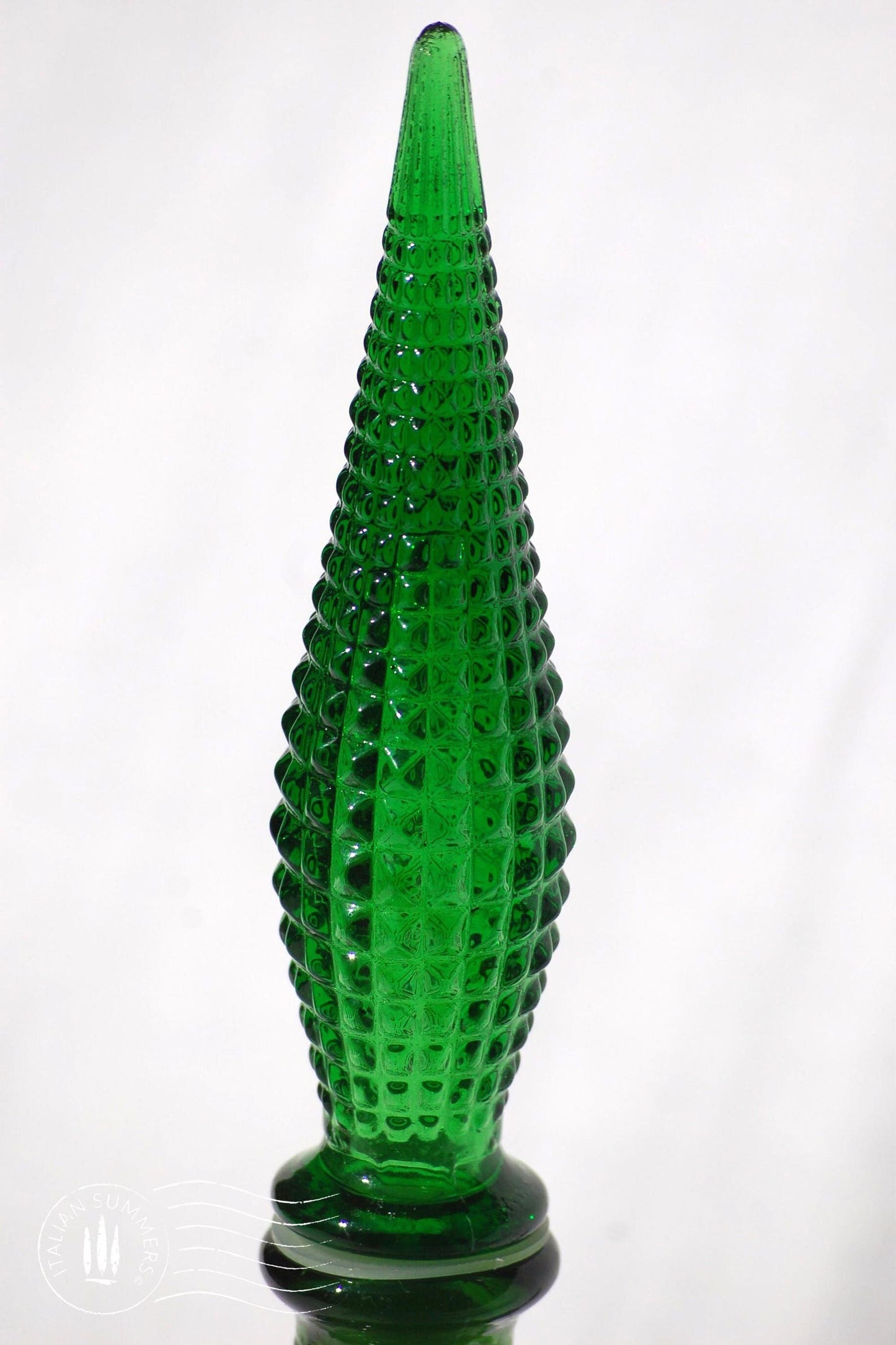 detail of a green Empoli Glass Genie Bottle stopper embossed with a diamonds pattern glistening in the sun against a white cloth background