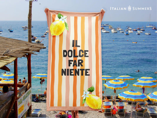 A retro-inspired Italian beach towel with pink and orange watercolor stripes, the phrase “Il Dolce Far Niente,” and two bright lemons in the corners—ideal for quick drying and an Italy vacation.