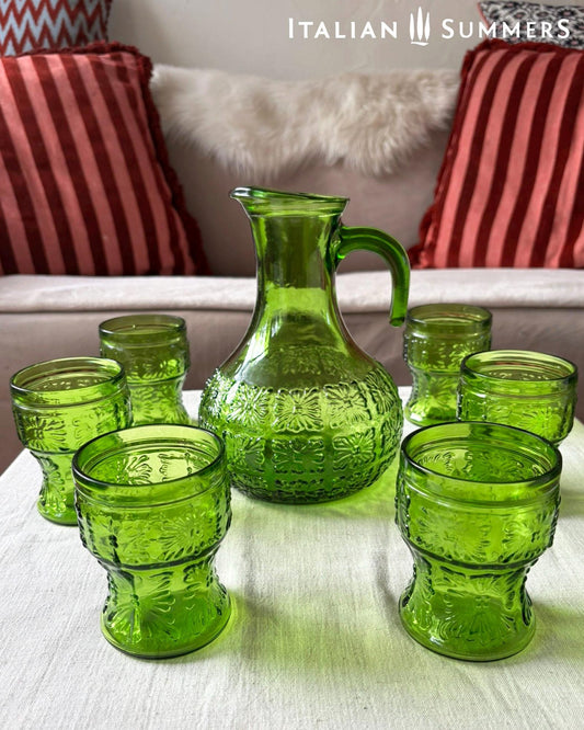 A green glass Italian carafe and six tumblers set on a white tablecloth