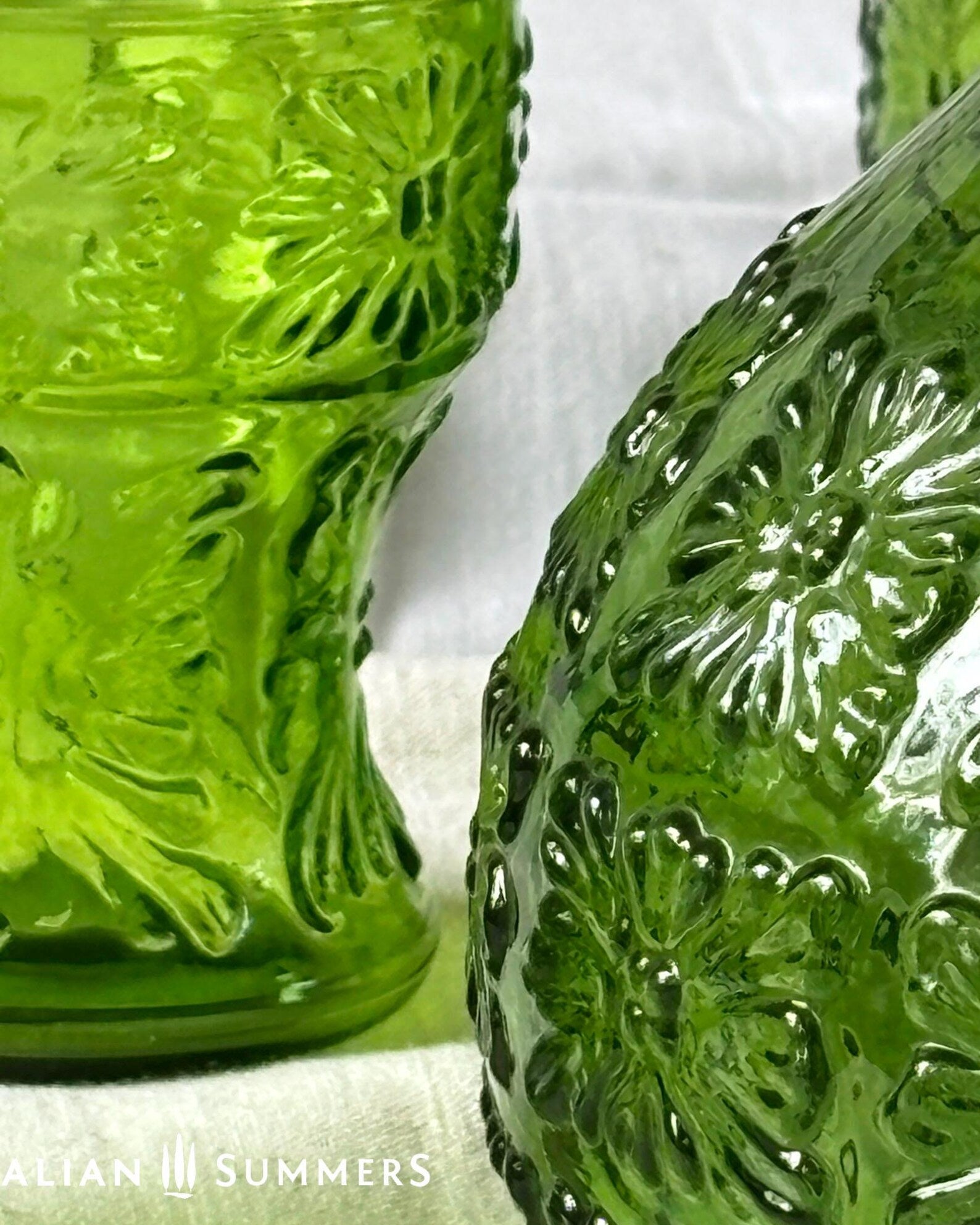 Detail of a green glass Italian carafe and six tumblers set on a white tablecloth