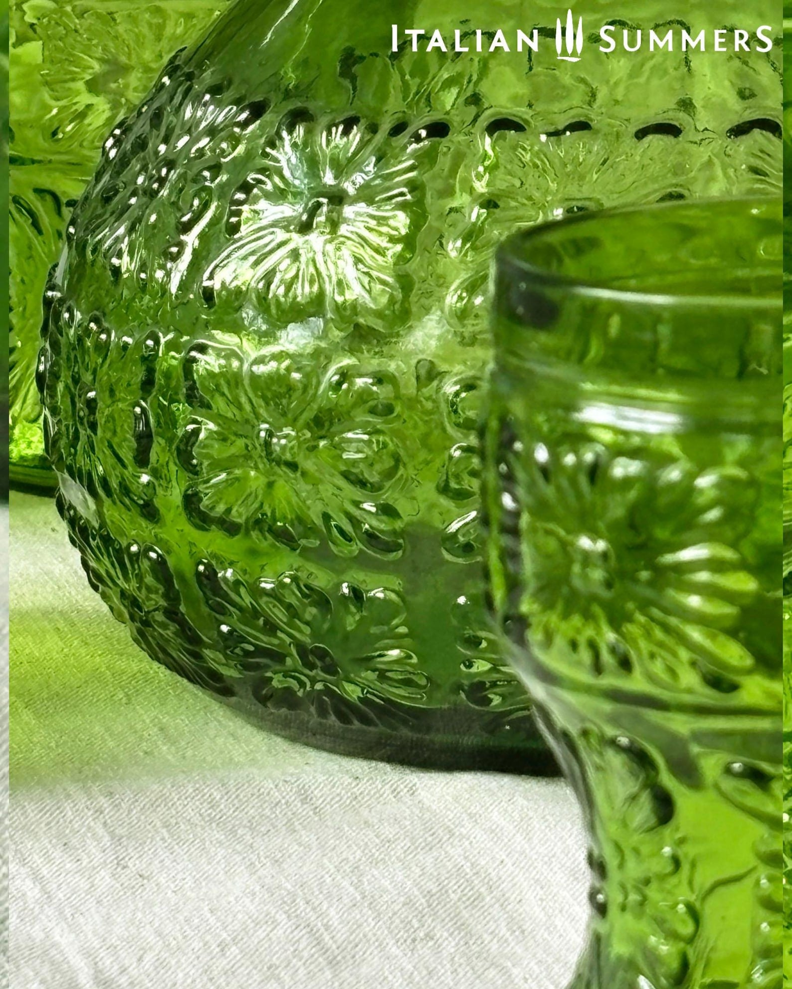 detail of a  green glass Italian carafe and six tumblers set on a white tablecloth