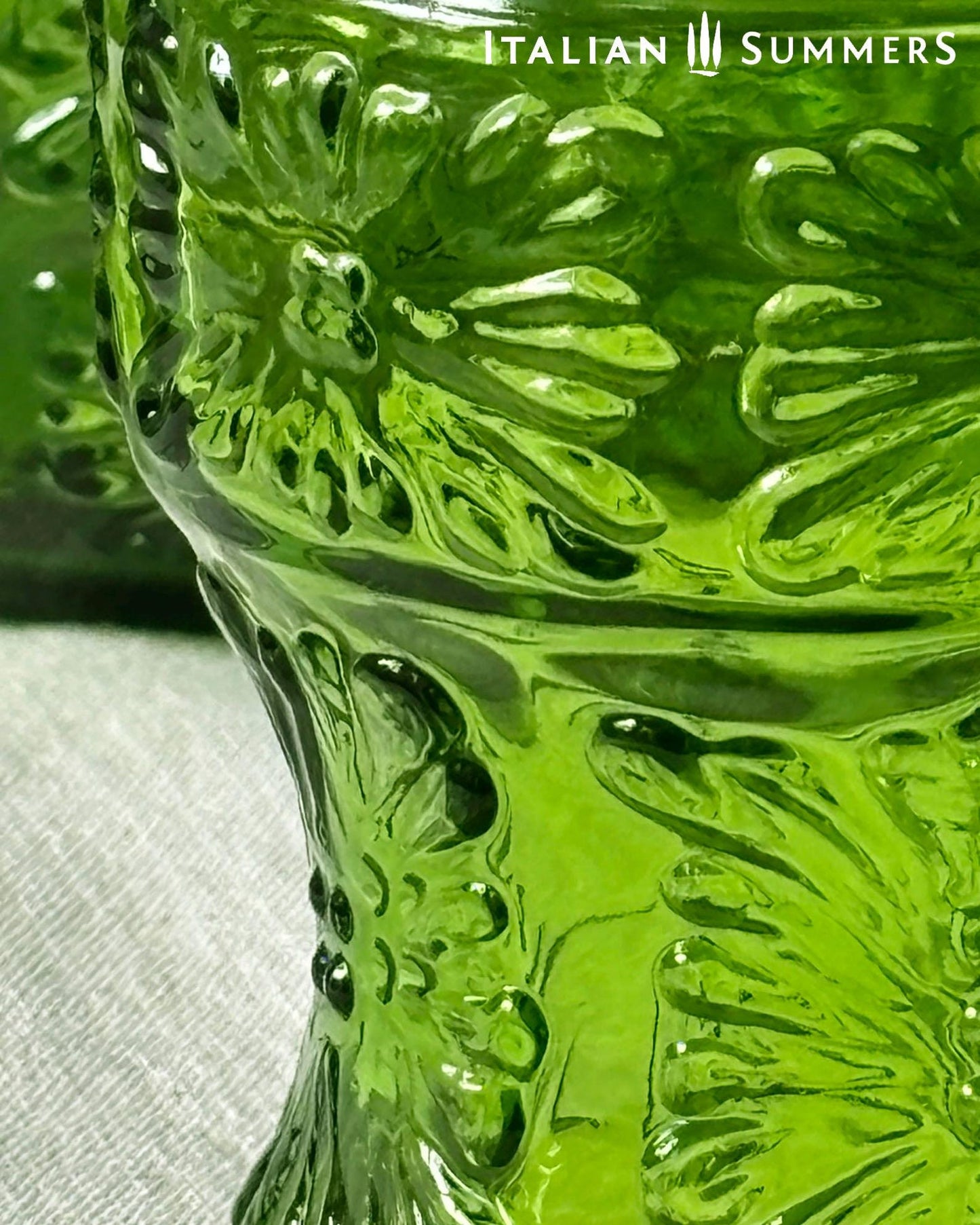 detail of a A green glass Italian carafe and six tumblers set on a white tablecloth