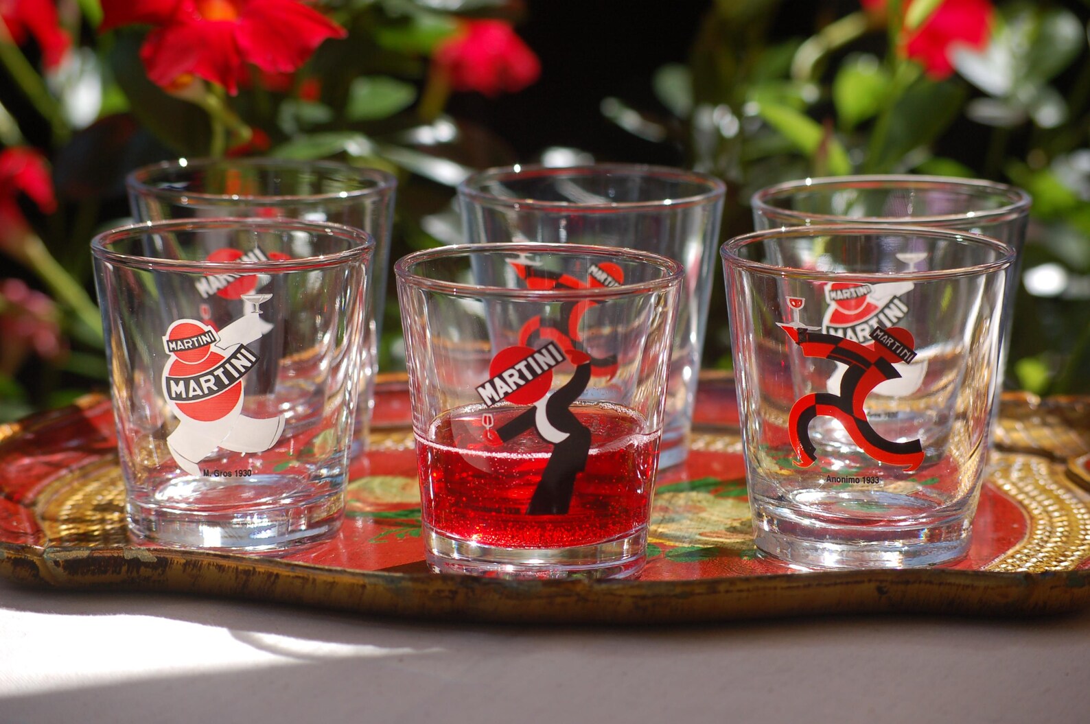 Set of Martini glasses with red liquid on a decorative tray outdoors.