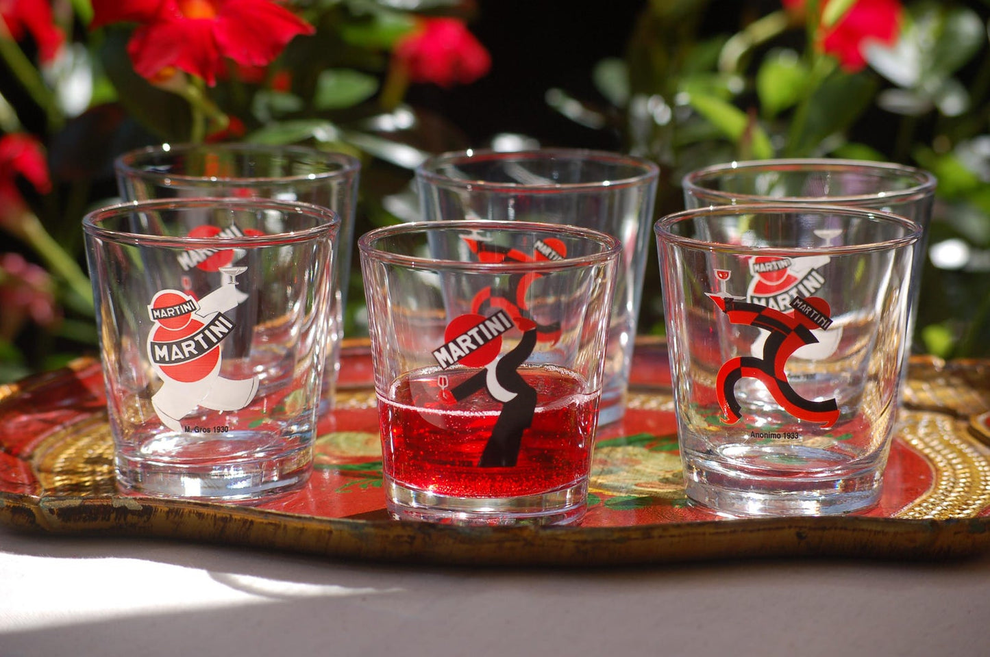 Set of Martini-themed tumbler glasses on a decorative tray with flowers in the background.