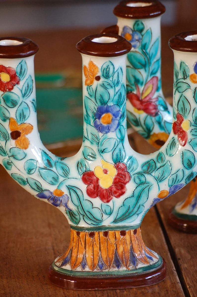A pair of colorful ceramic candleholders by Cerart Monaco  with floral design on a wooden surface