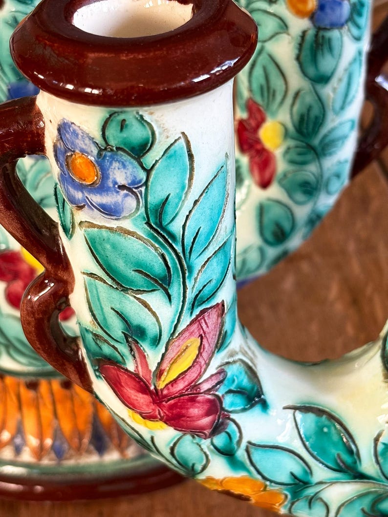 Ceramic candleholder with floral designs and brown handles on a wooden surface