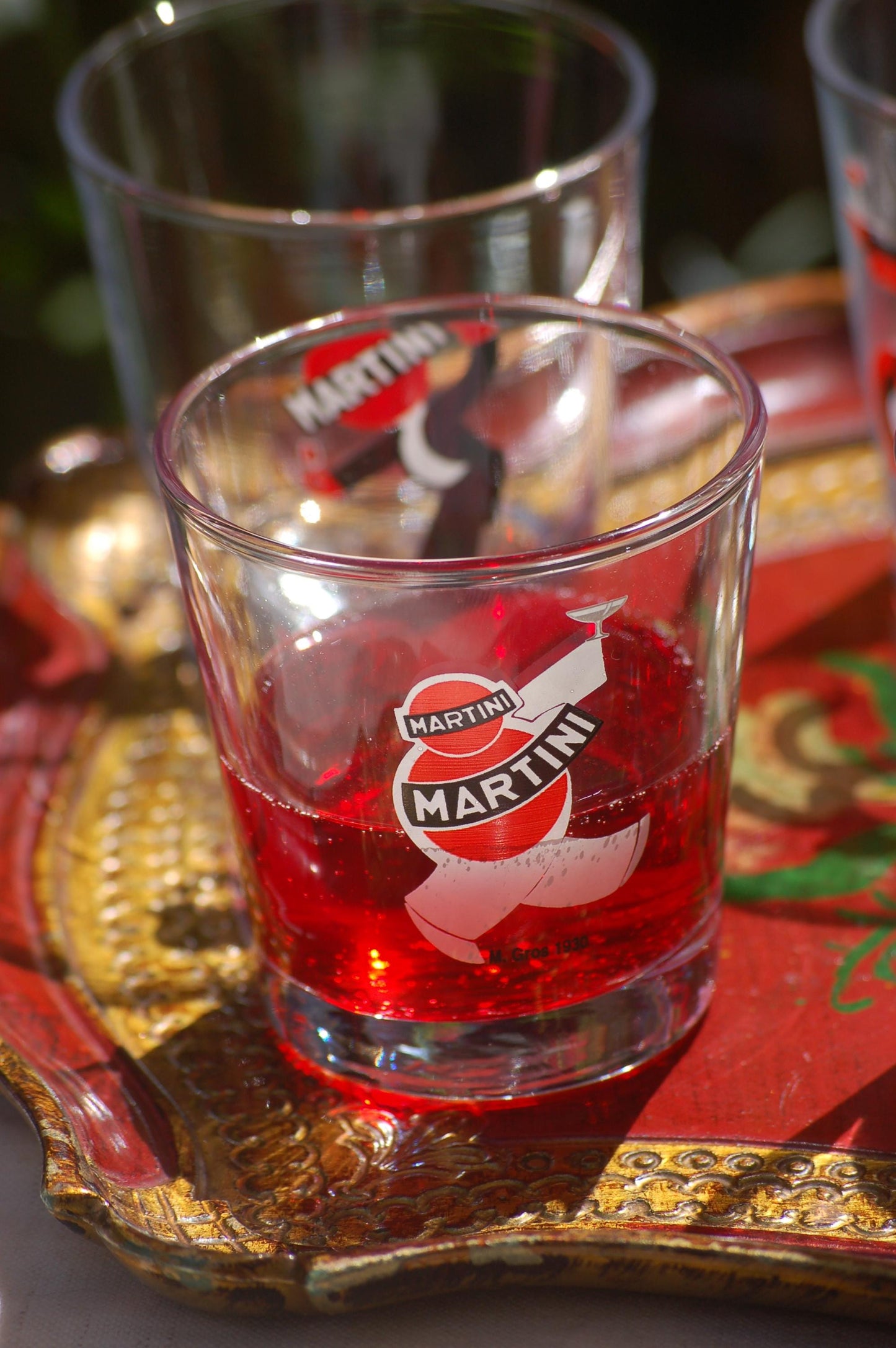 Clear glass with red liquid and Martini logo on a decorative tray