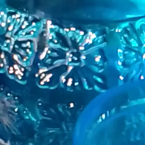 A blue vintage glass Italian carafe and six tumblers set on a blue an tablecloth white floral tablecloth in a garden setting.