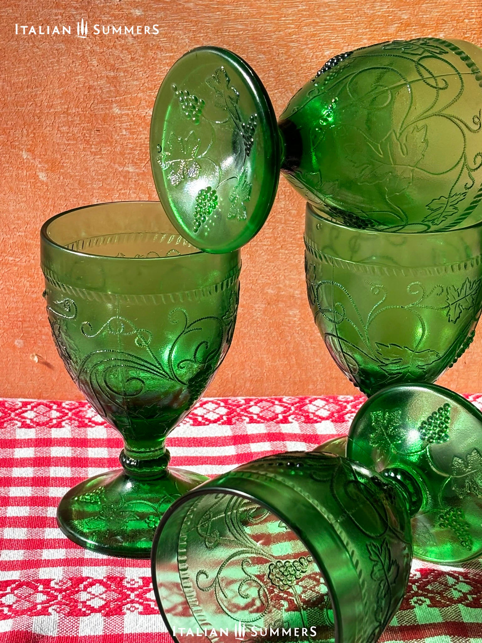 Green glass goblets with intricate designs on a red and white checkered tablecloth, branded 'Italian Summers'.