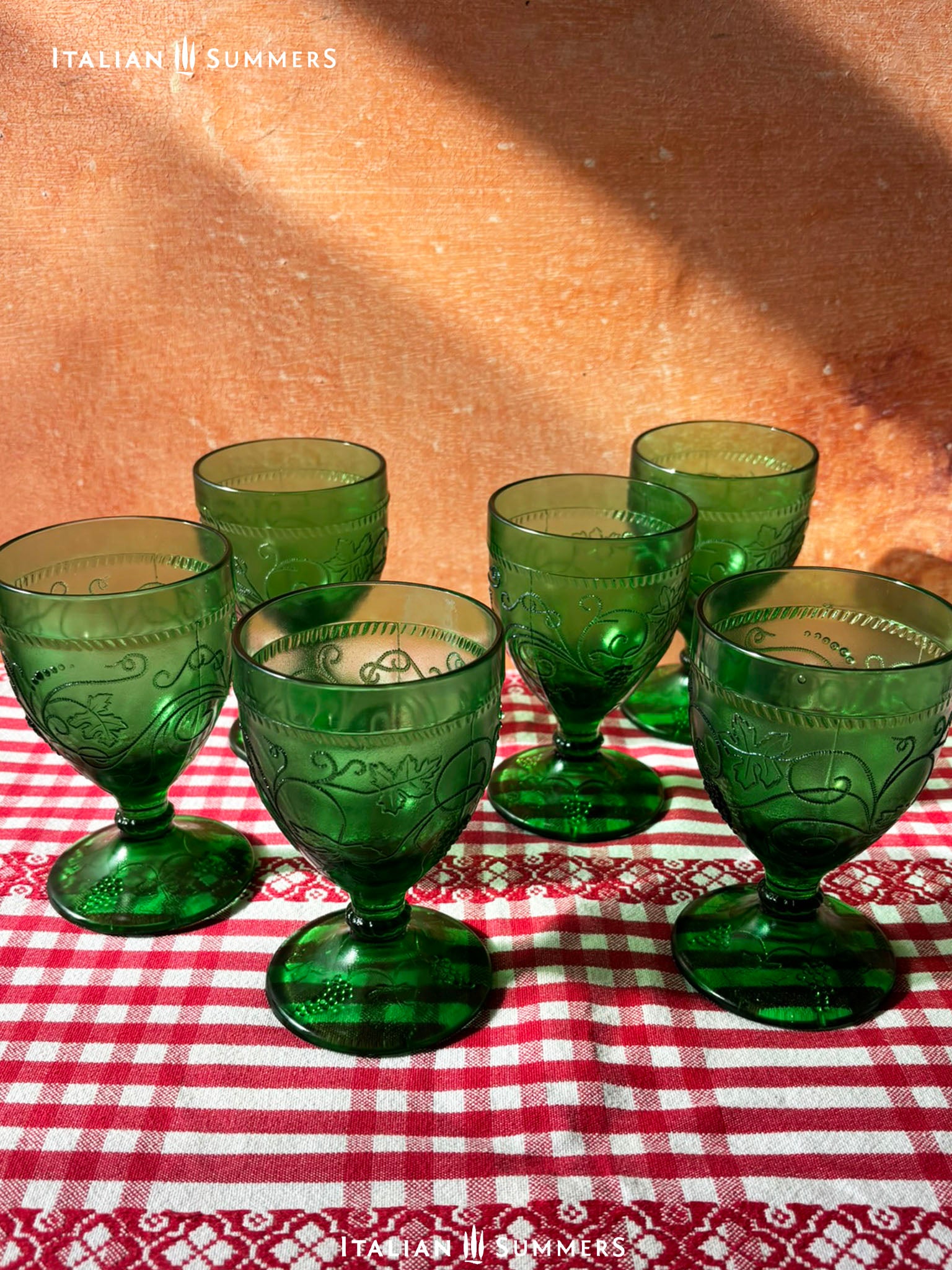 Set of green glass goblets on a red and white checkered tablecloth with 'Italian Summers' branding.