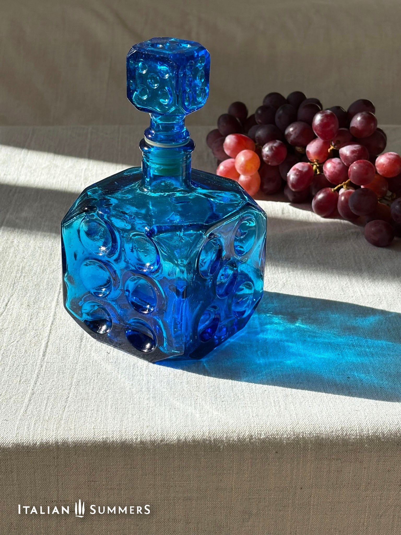Sapphire Empoli dice glass decanter on a light background with red grapes