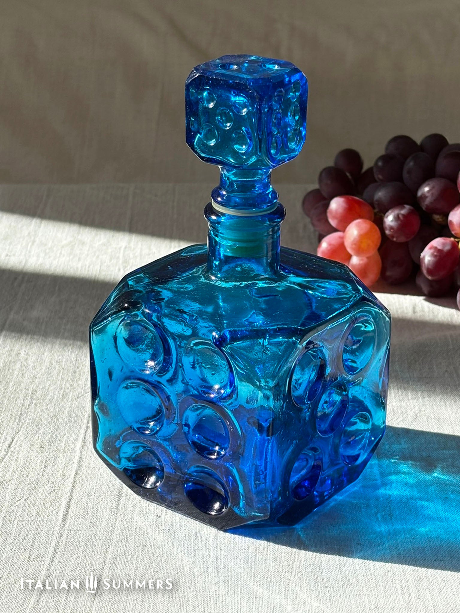 Sapphire blue Empoli dice glass decanter on a light background with red grapes