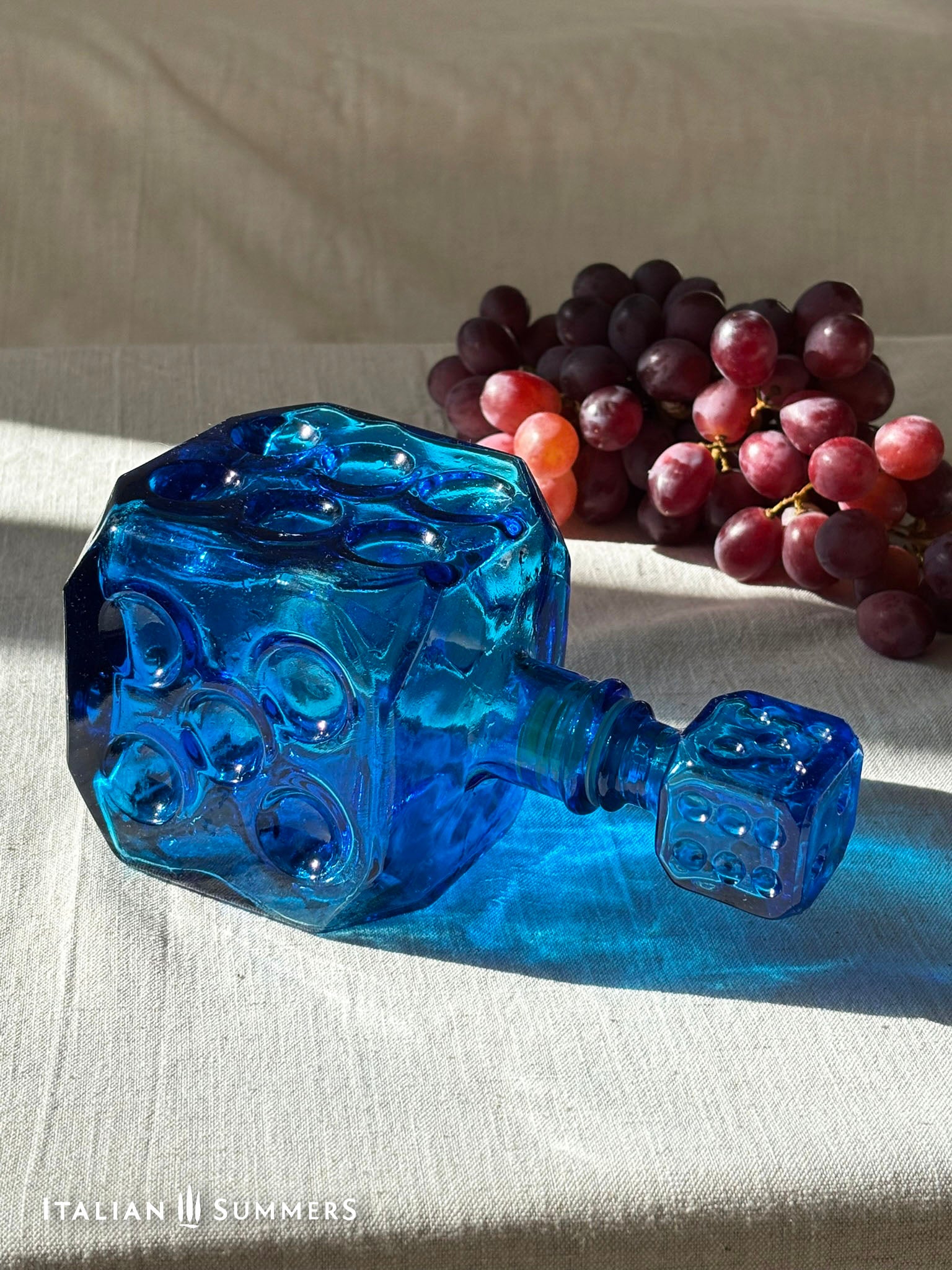 Sapphire blue Empoli dice glass decanter on a light background with red grapes