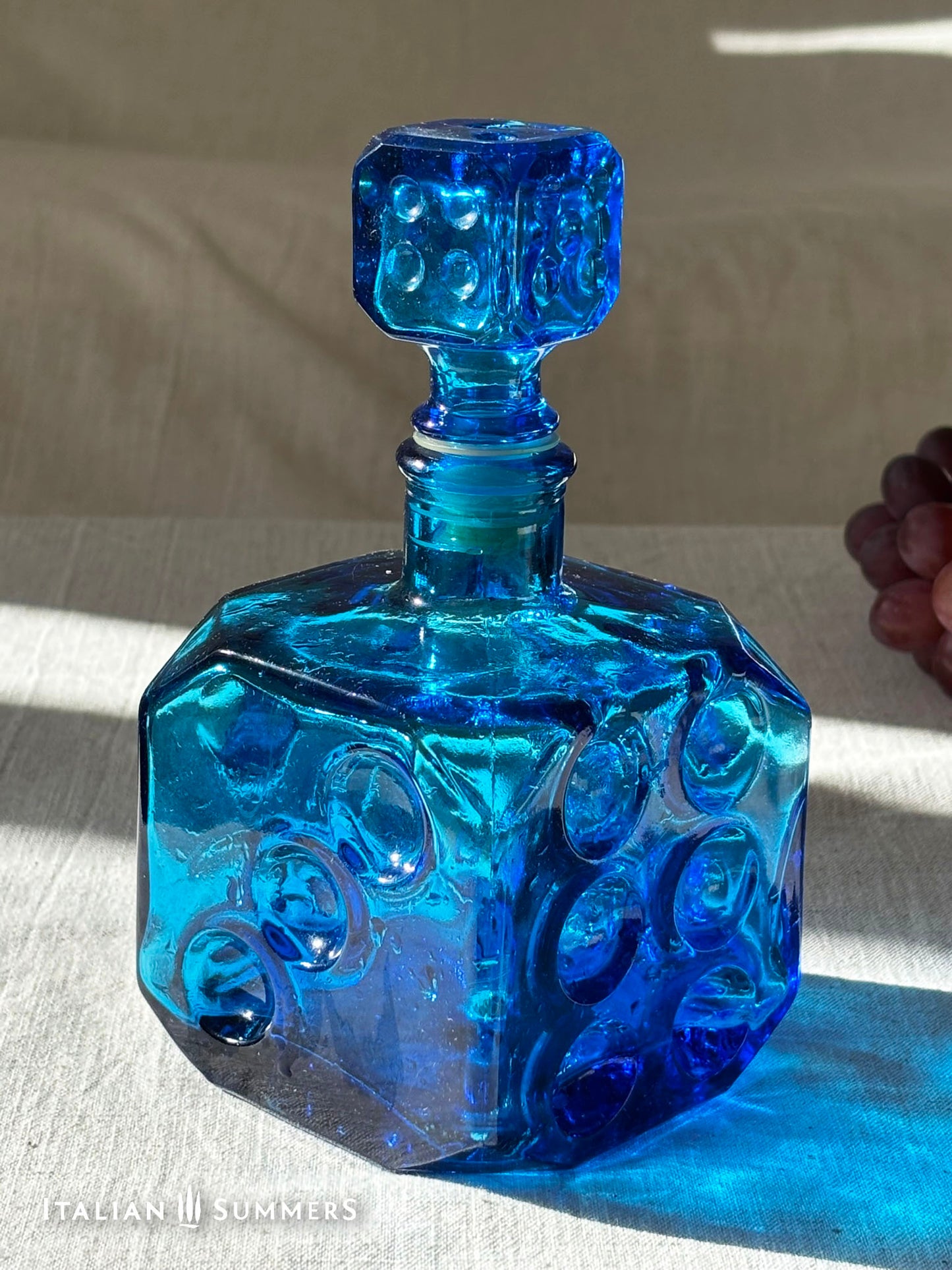 Sapphire blue Empoli dice glass decanter on a light background with red grapes