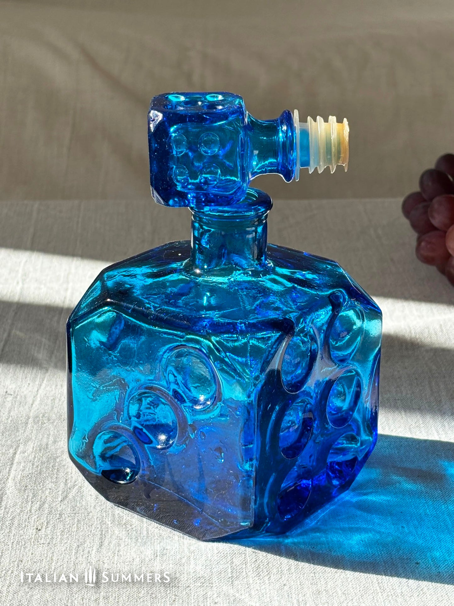 Sapphire blue Empoli dice glass decanter on a light background with red grapes