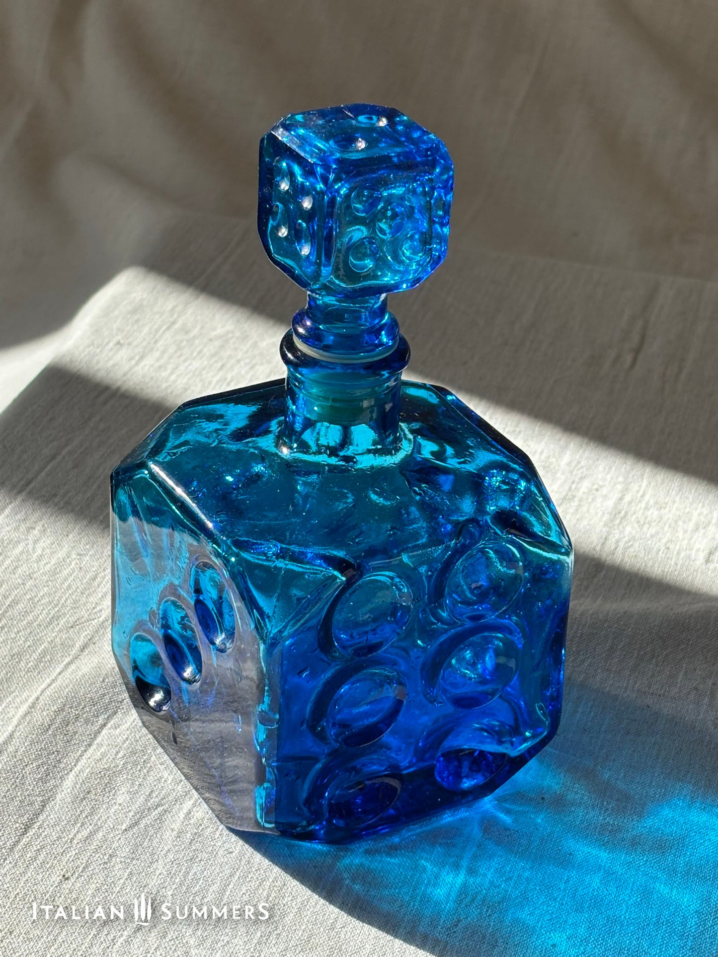 Sapphire blue Empoli dice glass decanter on a light background with red grapes