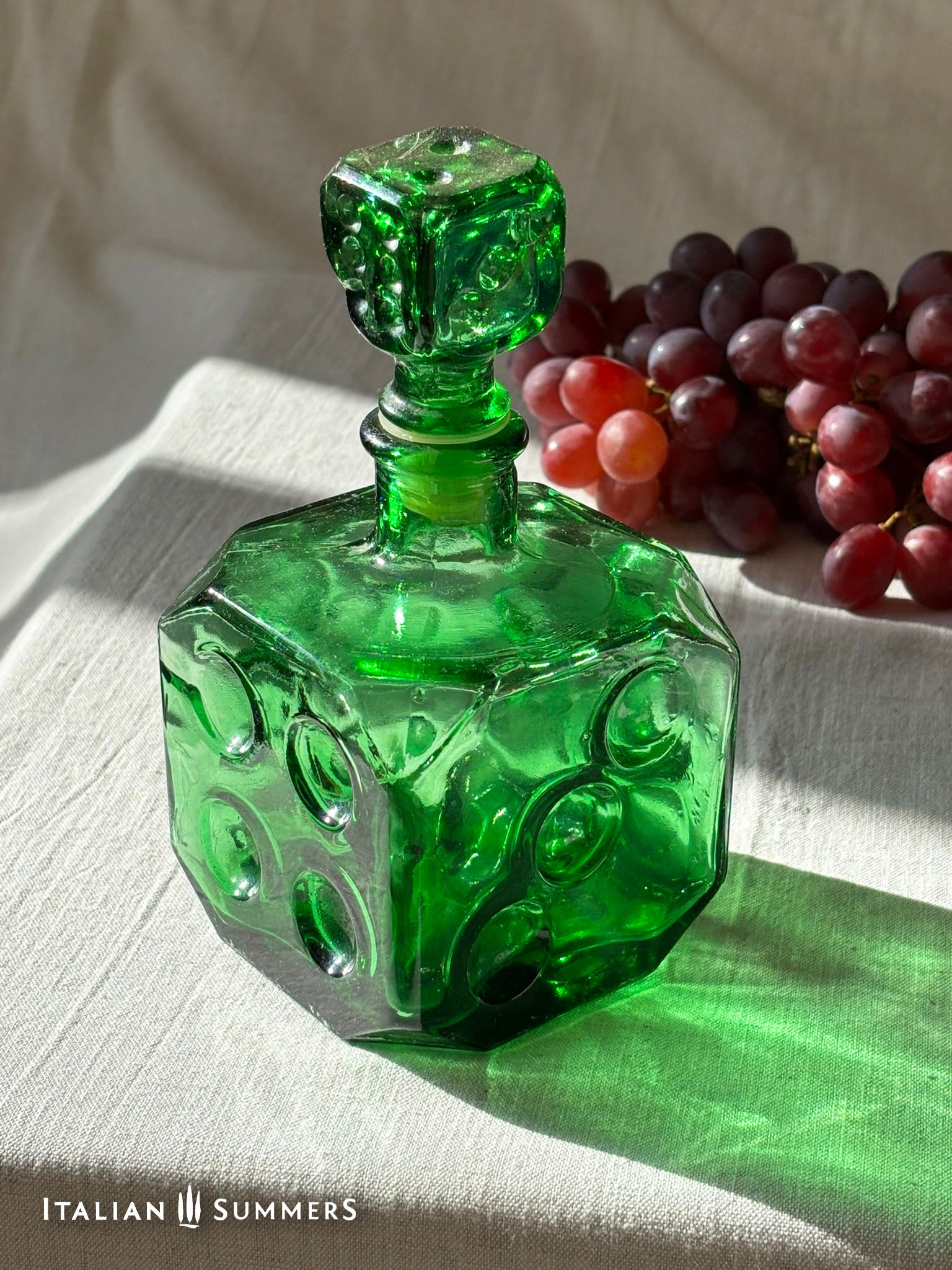 Emerald Green Empoli dice glass decanter on a light background with red grapes
