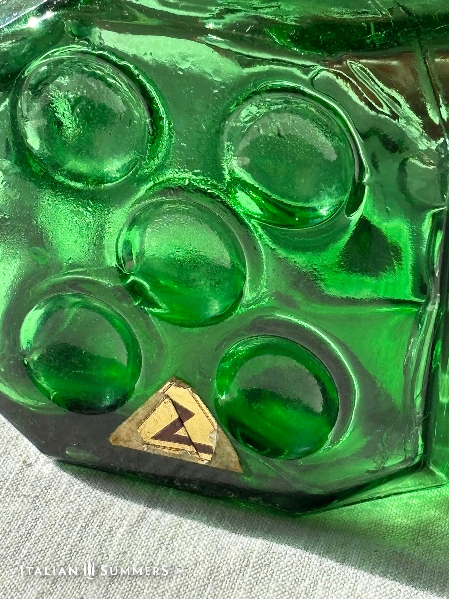Close-up of an Emerald Green Empoli dice glass decanter and a gold triangle label.