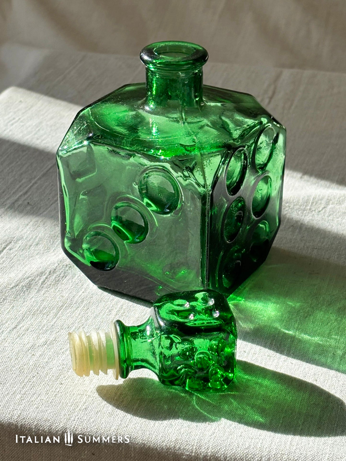 Emerald Green Empoli dice glass decanter on a light background with the glass stopper and nylon insert lying sideways on the white surface 