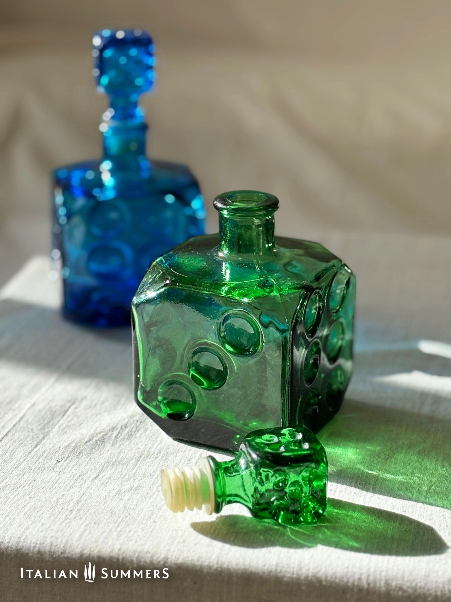 Green and blue glass bottles on a textured surface with 'Italian Summers' branding.
