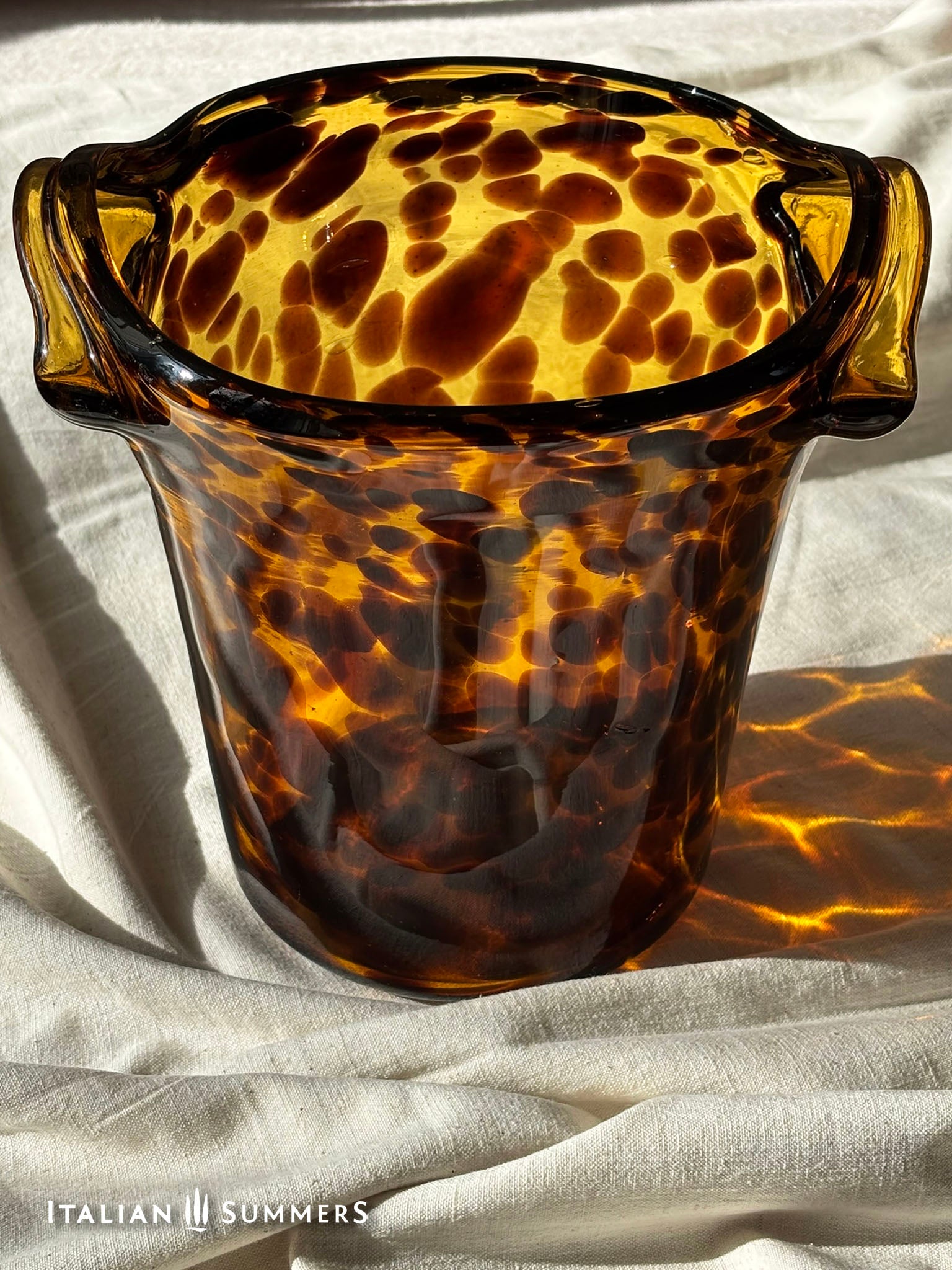 Tortoiseshell patterned glass ice bucket on a light fabric background