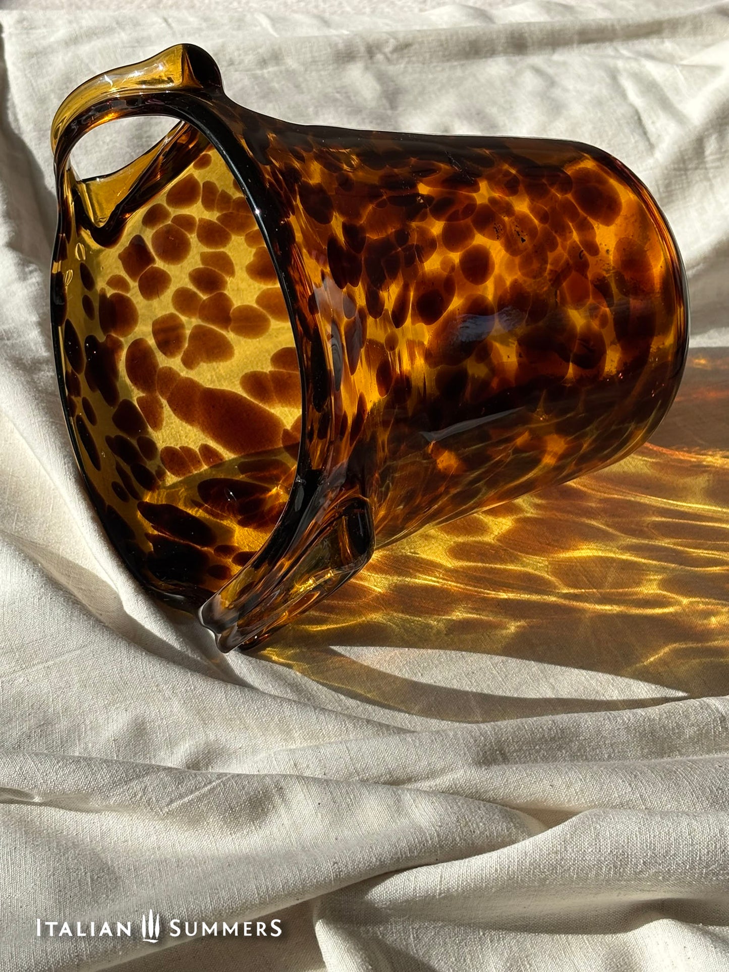 Tortoiseshell-patterned glass vase on a textured white surface with 'Italian Summers' branding.