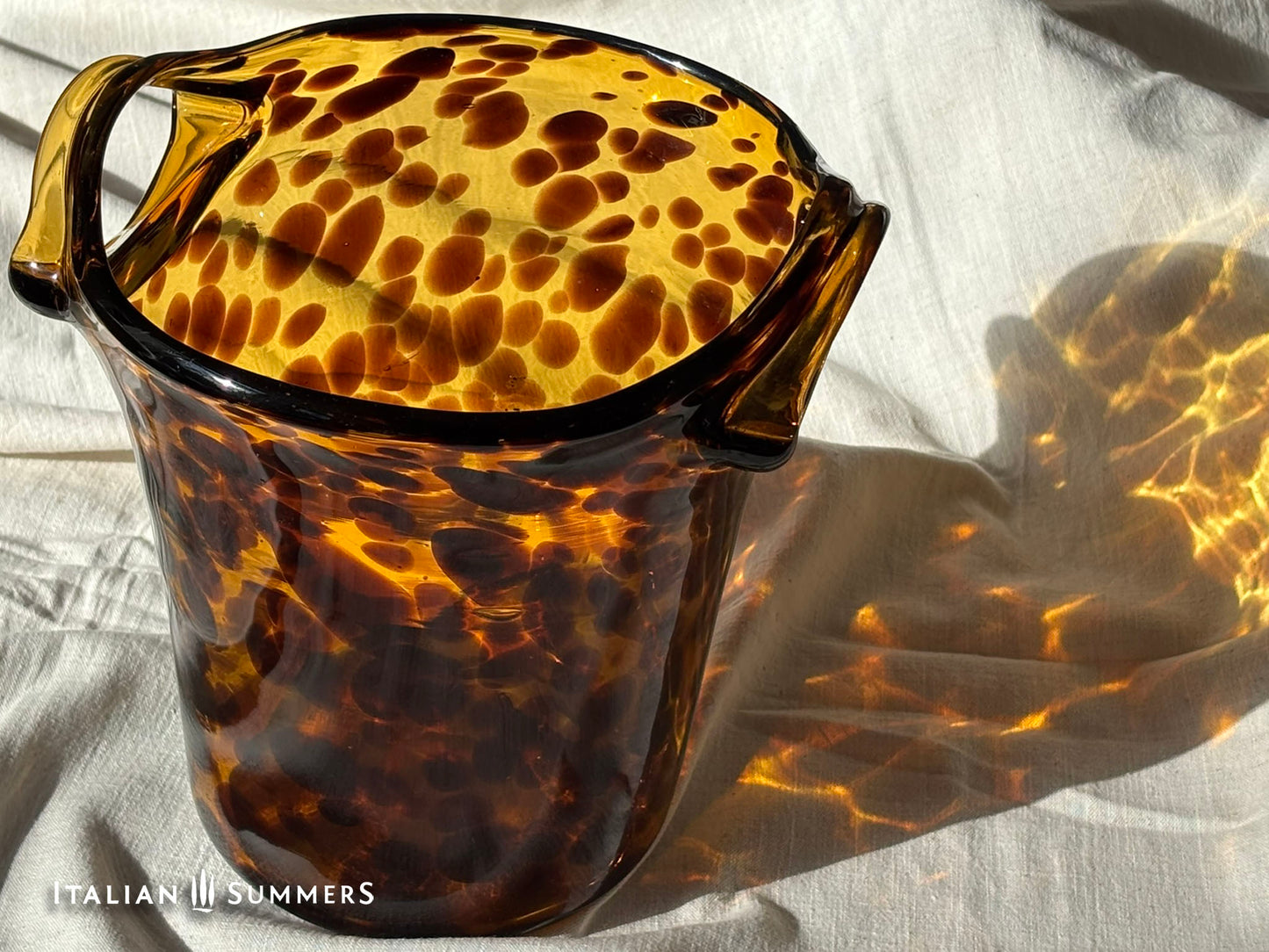 Tortoiseshell patterned glass ice bucket on a light fabric background